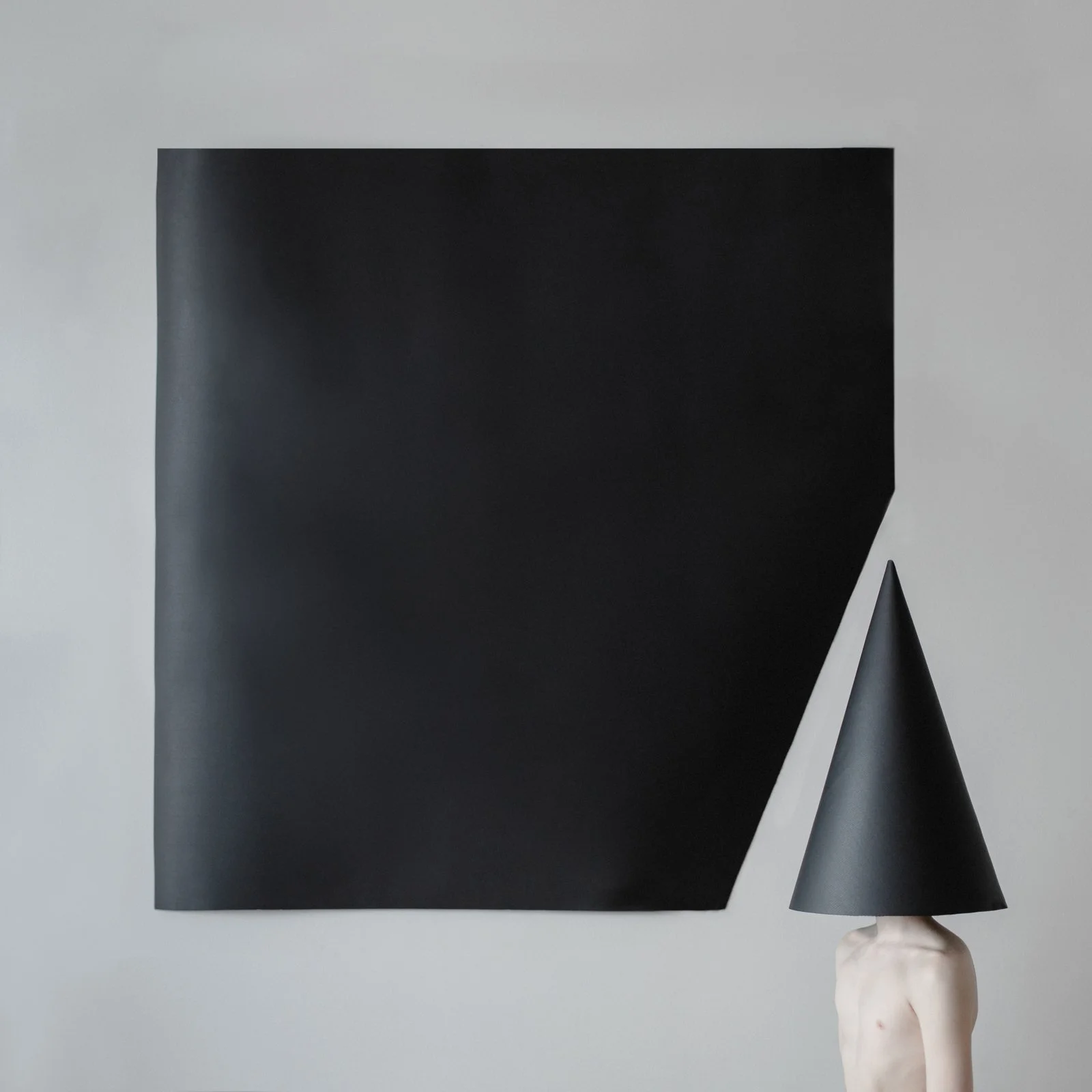 Facing left standing man is hiding his head with a black cone below a black concentric inner square of a light gray square.
