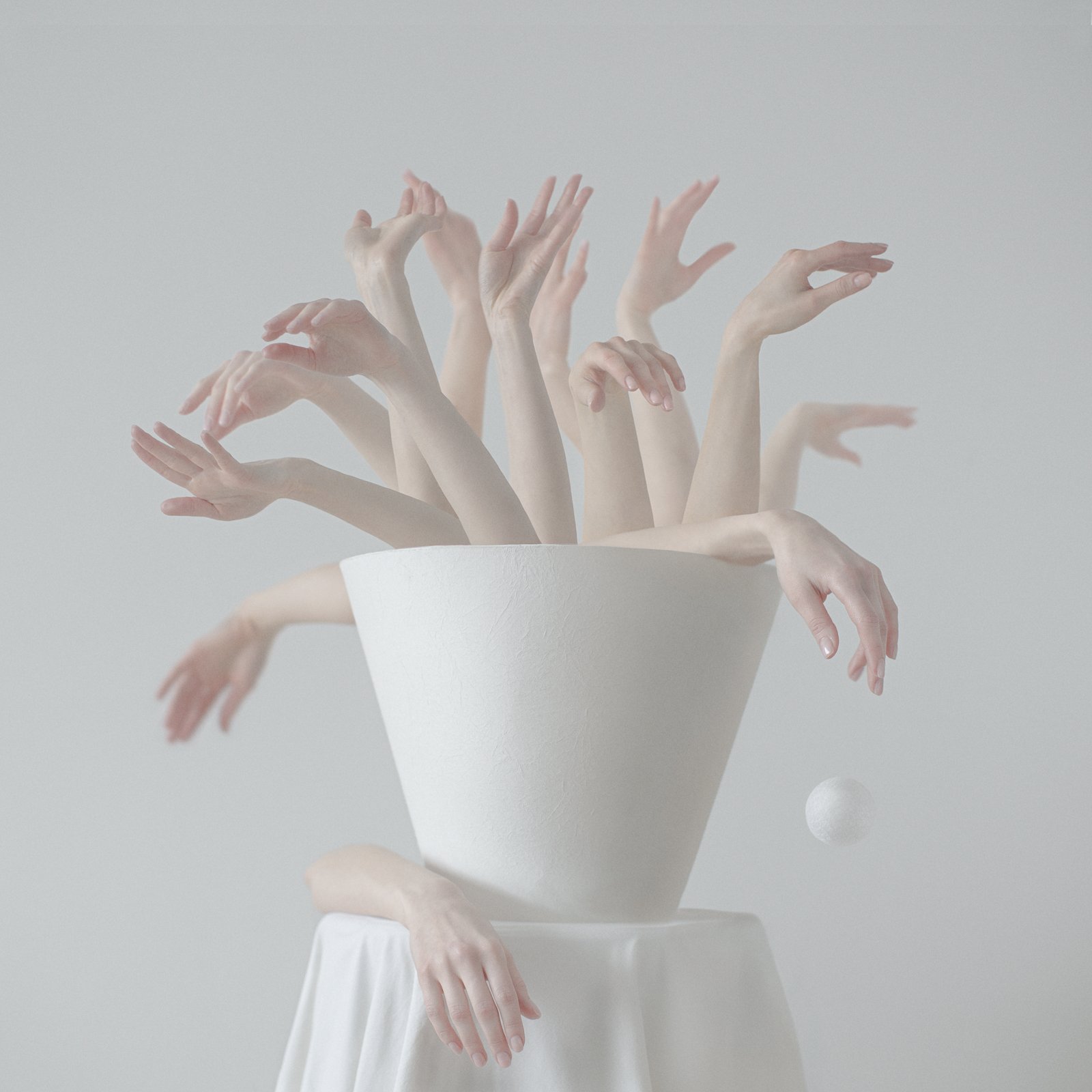 Lower round white tablecloth holding a white conical flower vase full of a light skin arms bush within a light gray background.