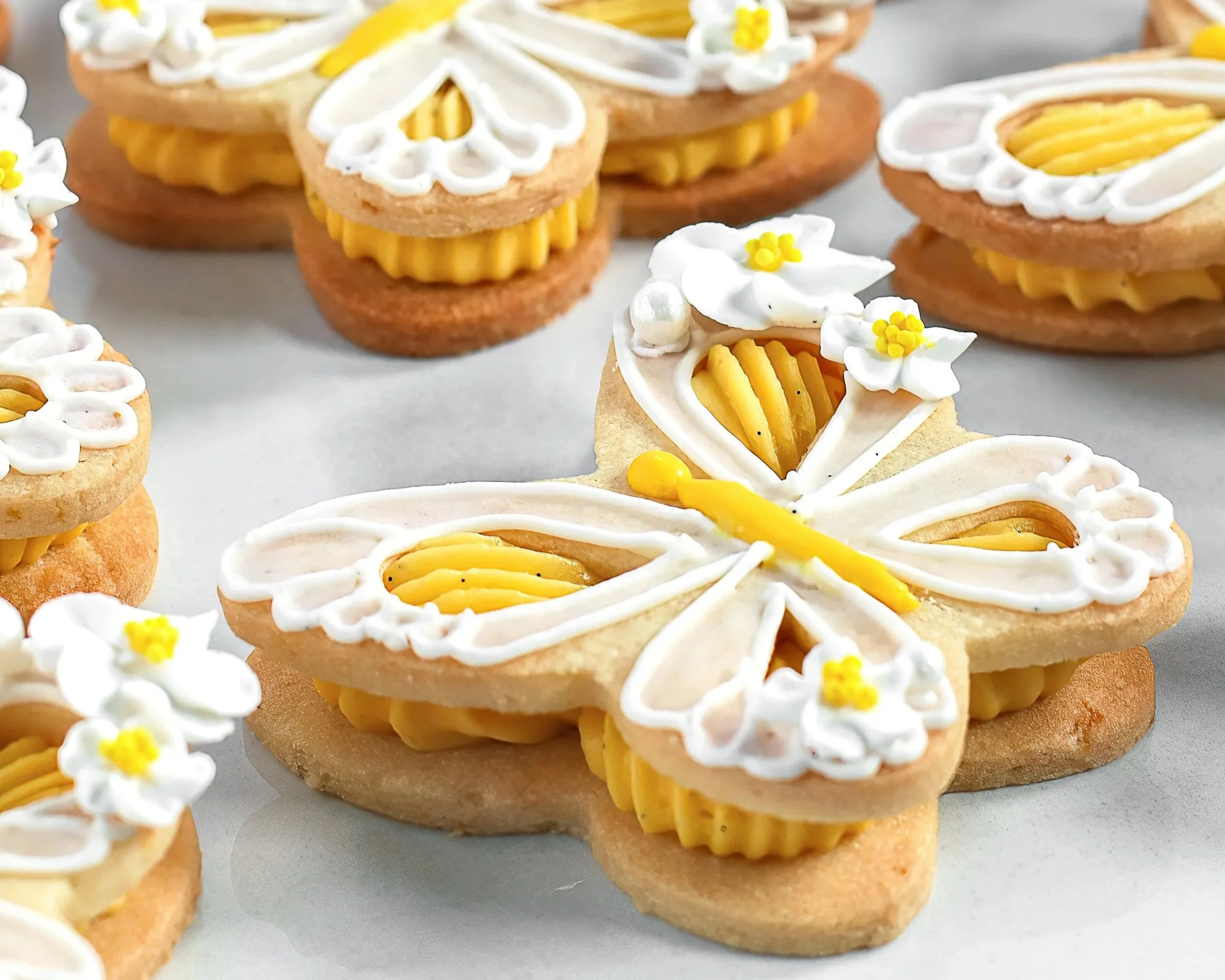 Close look at decorated lemon butterfly cookies with lace-style royal icing and tiny sugar flowers.