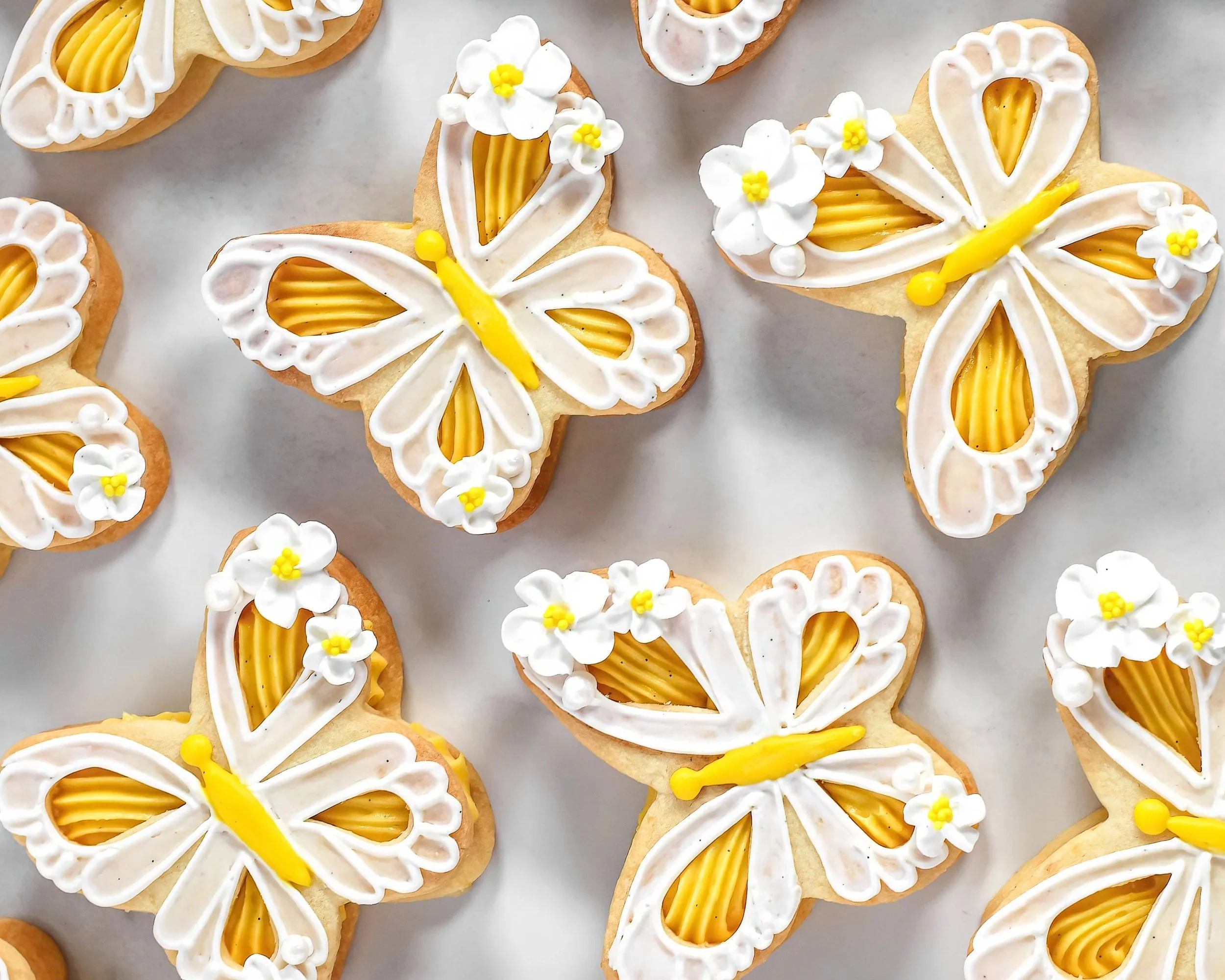 Overhead view of lemon butterfly cookies with white chocolate lemon curd filling and delicate royal icing lace and flowers.