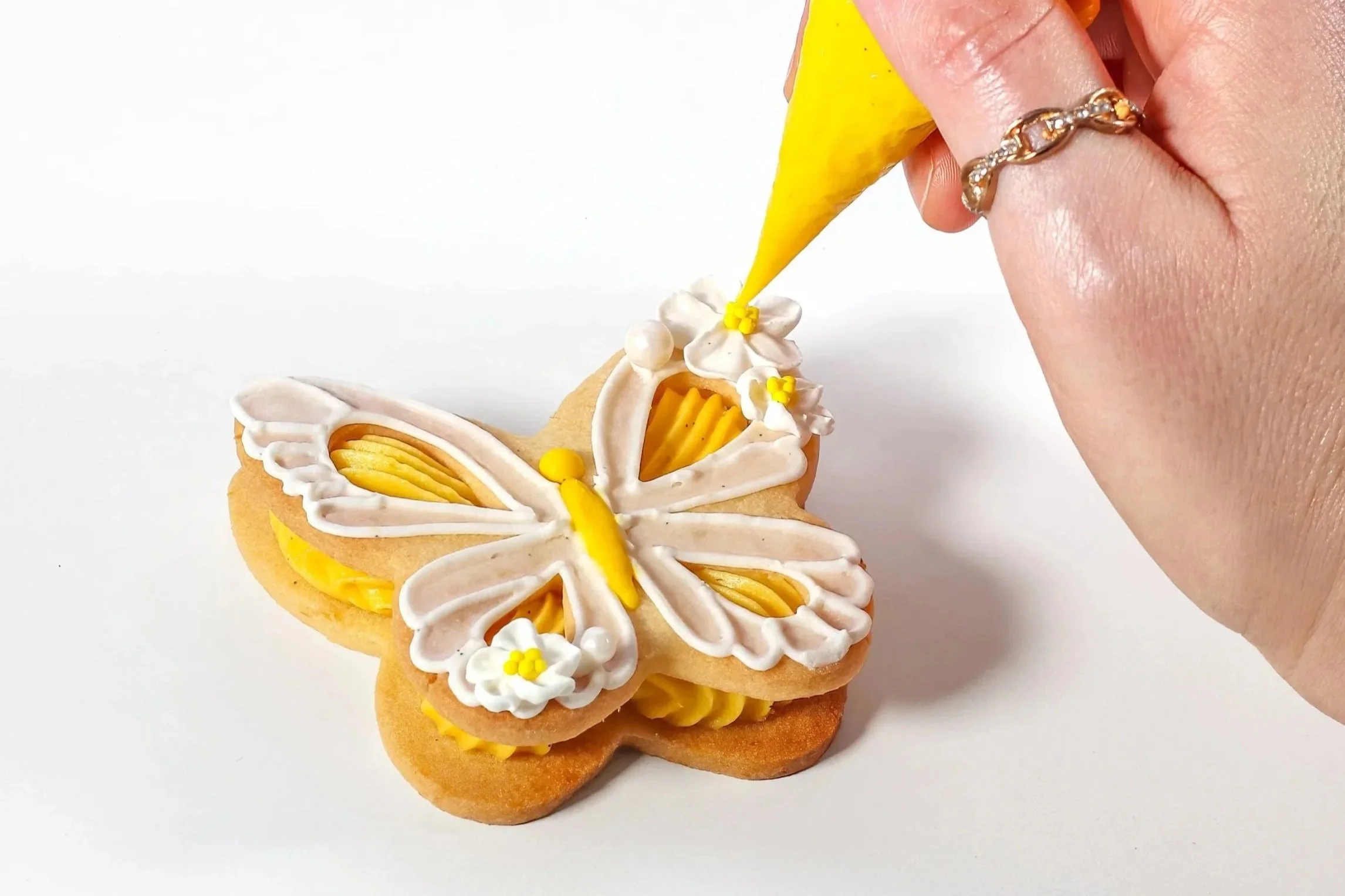 Close-up of a hand piping royal icing lace onto a decorated lemon butterfly cookie.