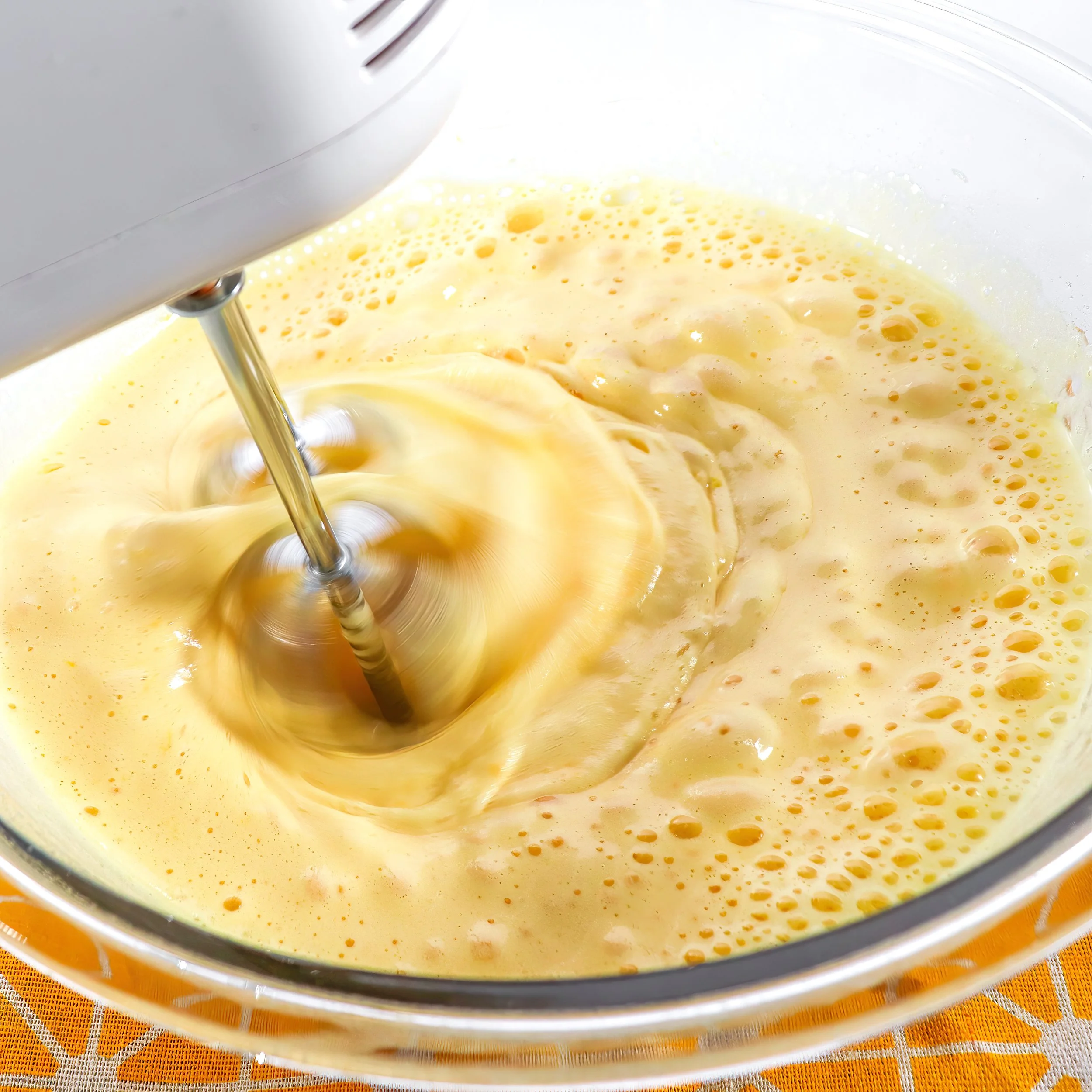 Midway through whipping the egg and sugar mixture, showing a bubbly, airy consistency before reaching ribbon stage.