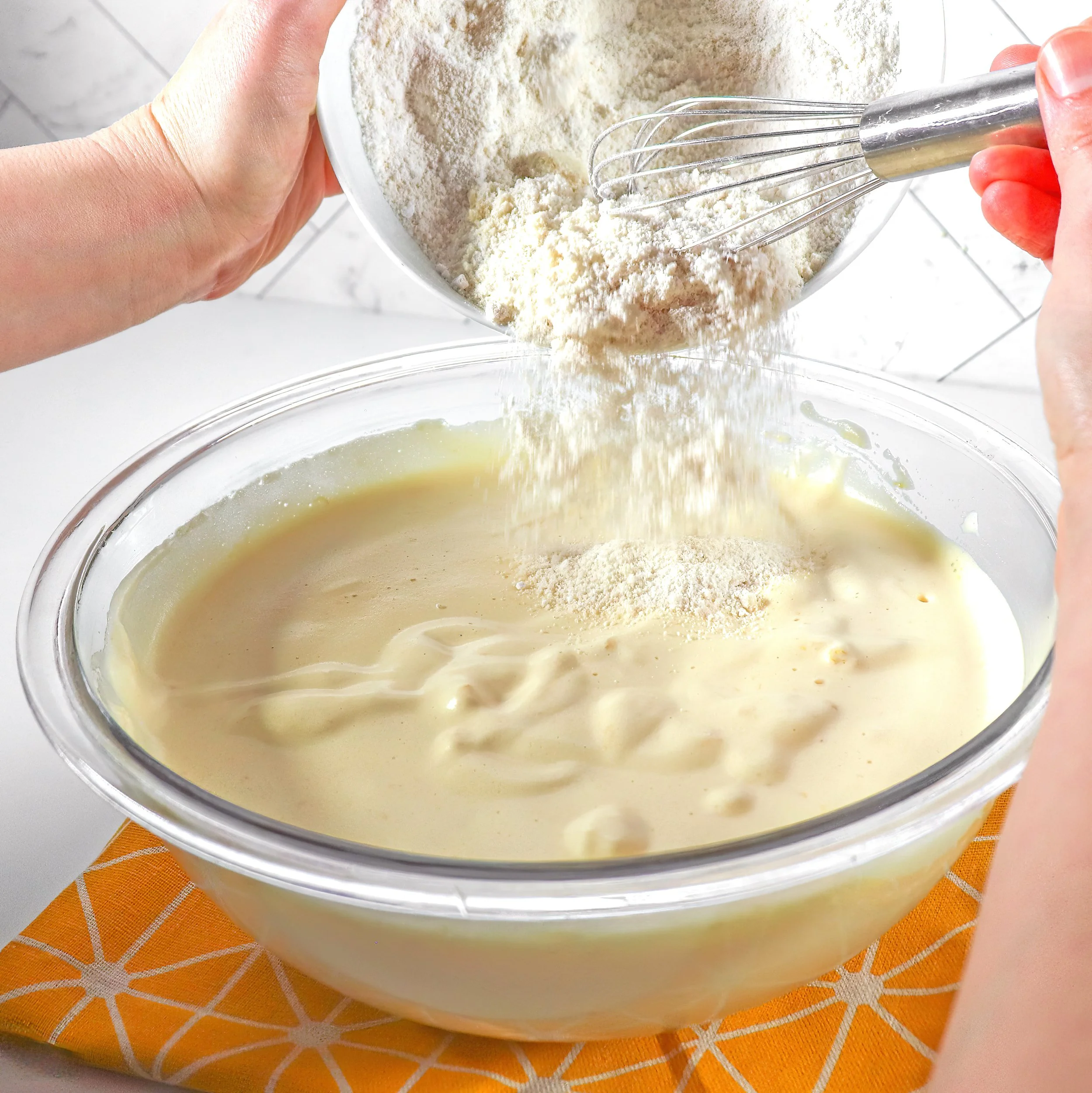 Flour and almond flour being gently folded into the lemon sponge batter to maintain its airy texture.