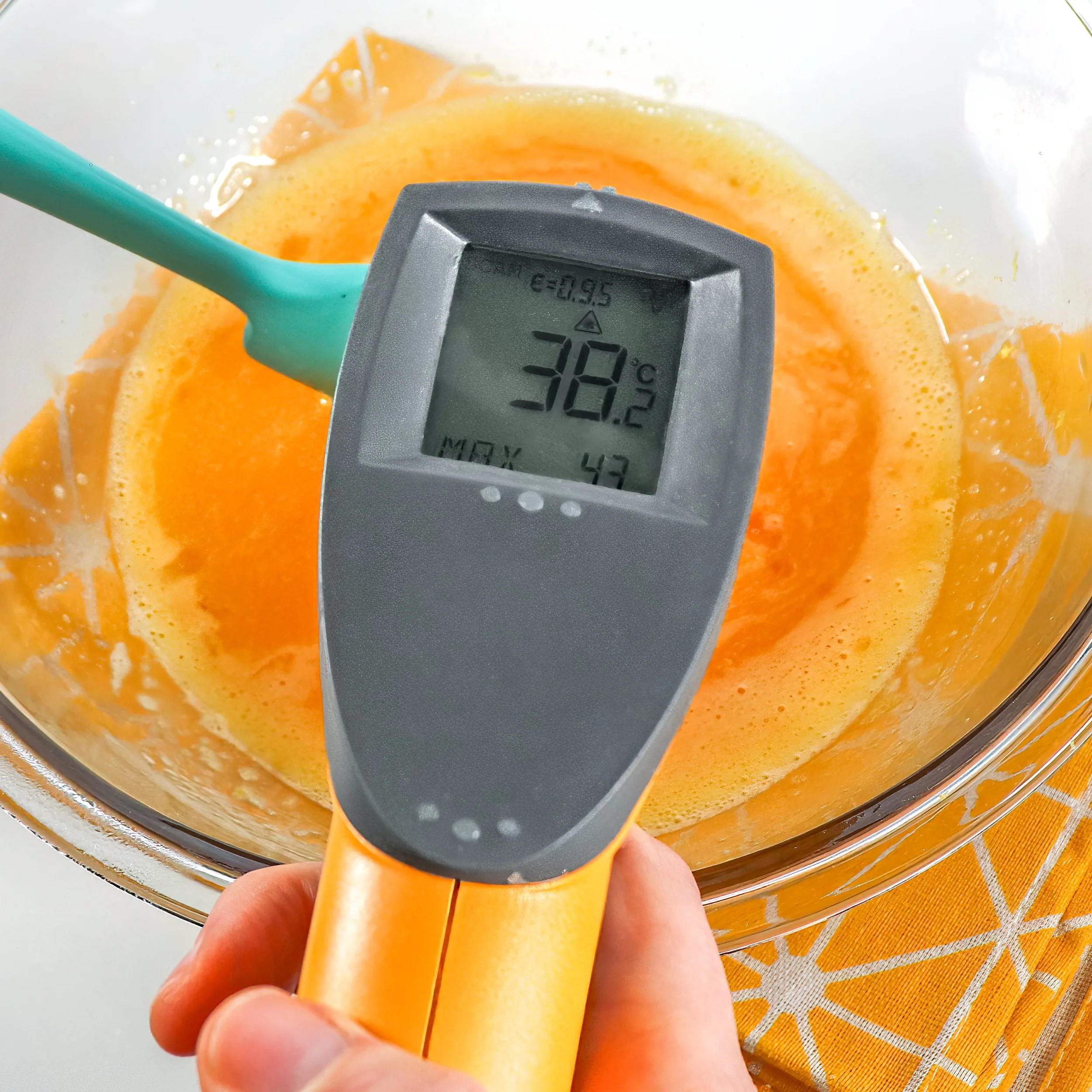 Close-up of a laser thermometer checking the temperature of a gently-heated egg and sugar mixture, reaching 38–40ºC for optimal whipping.