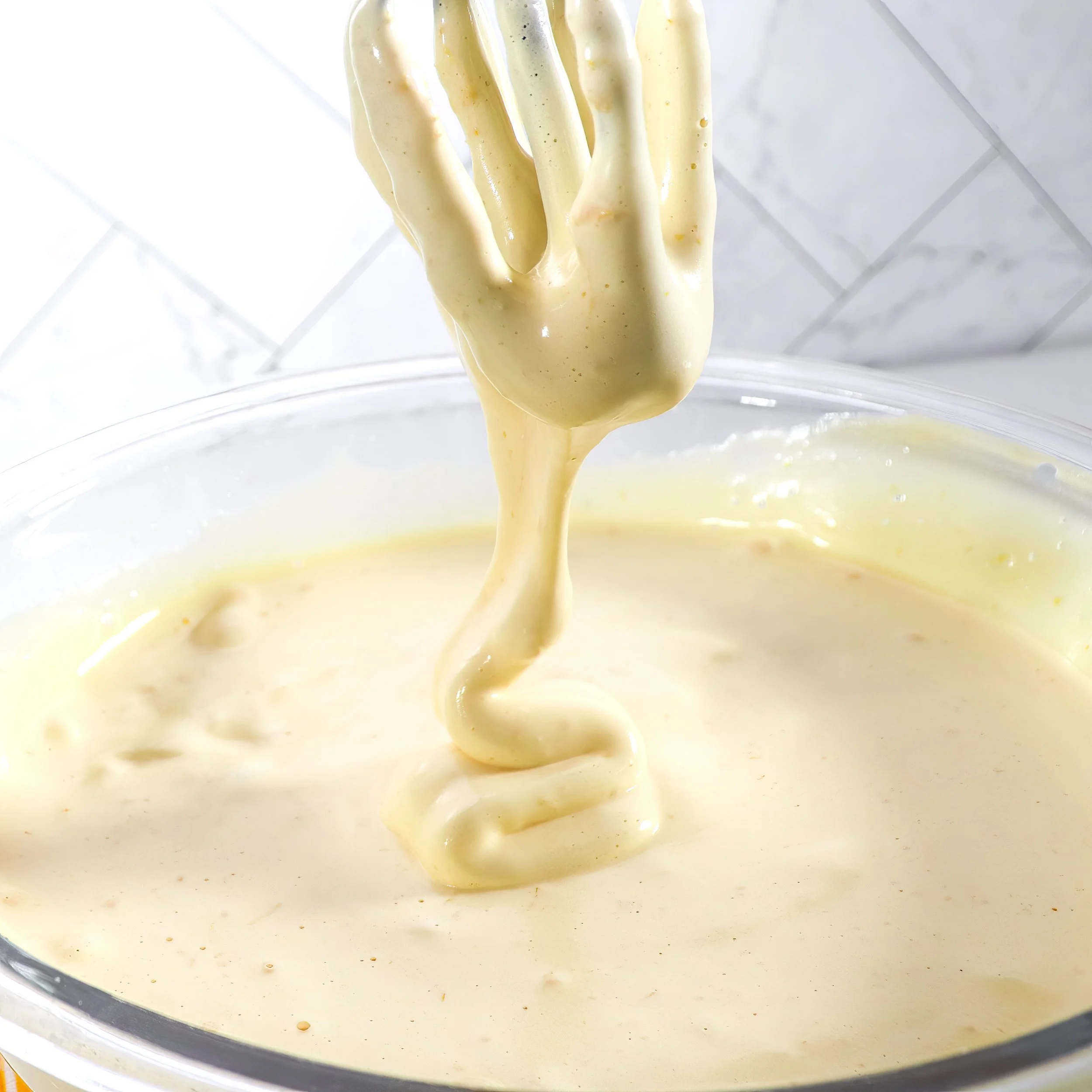 Close-up of lemon sponge batter at ribbon stage, with thick trails that hold their shape before slowly dissolving back into the surface.