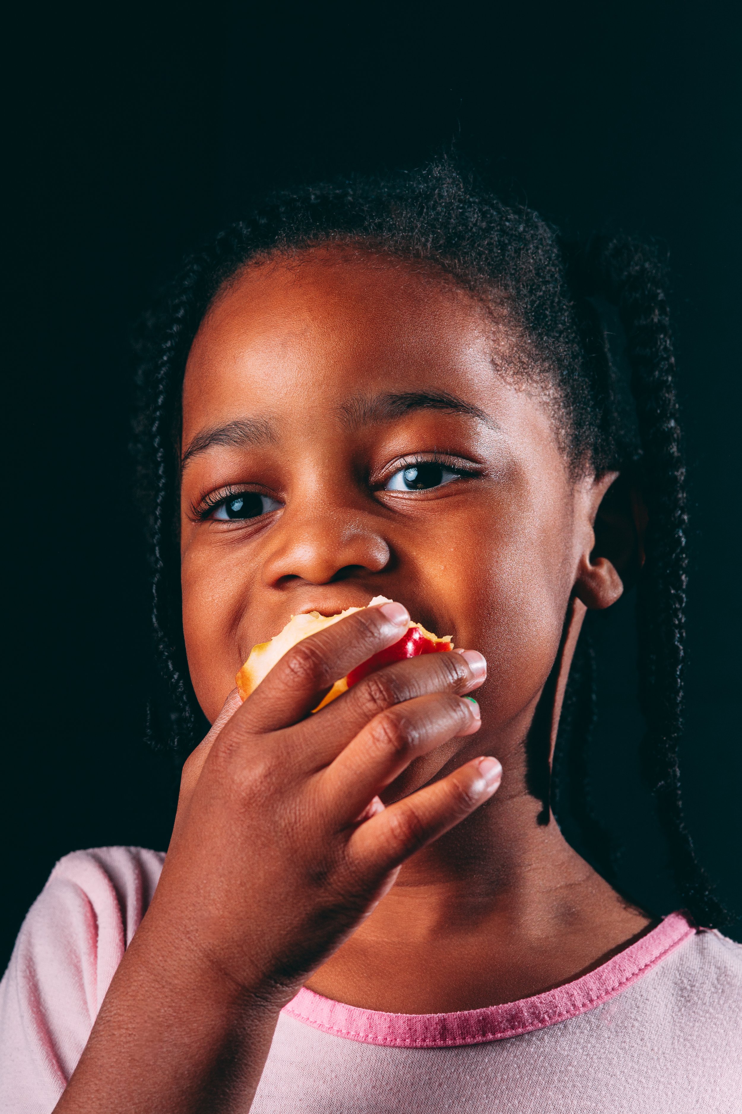 Young girl with dark hair and brown skin eating an apple.