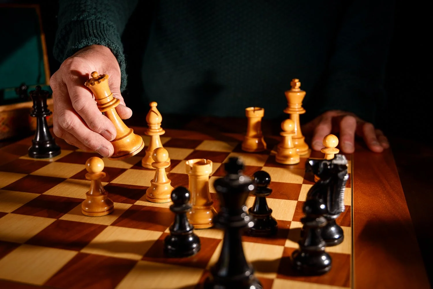 Close-up of a person moving a chess piece on a wooden chessboard with black and white pieces.