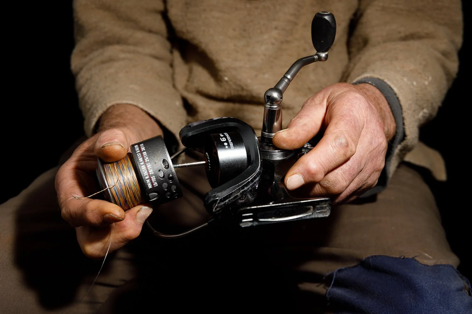 Person holding a fishing reel with multicolored fishing line, adjusting or preparing it for fishing.