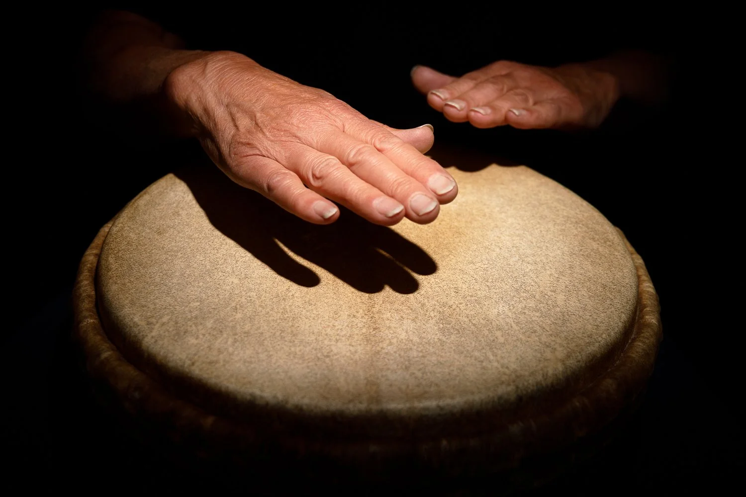 Person's hands playing a traditional drum with a shadow cast on it.