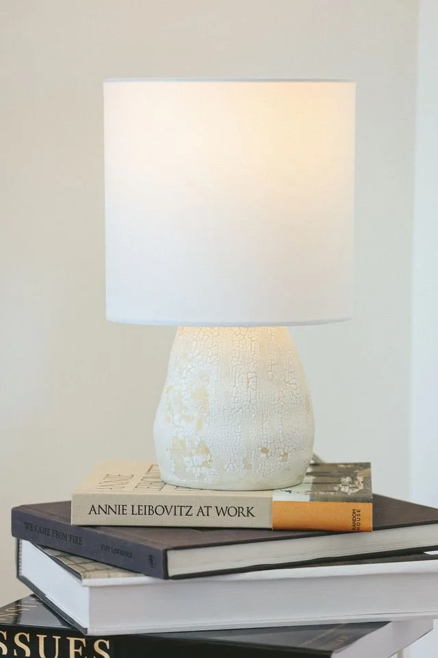 A white lamp with a textured base made by Natalya Jane on top of a stack of books on a table.