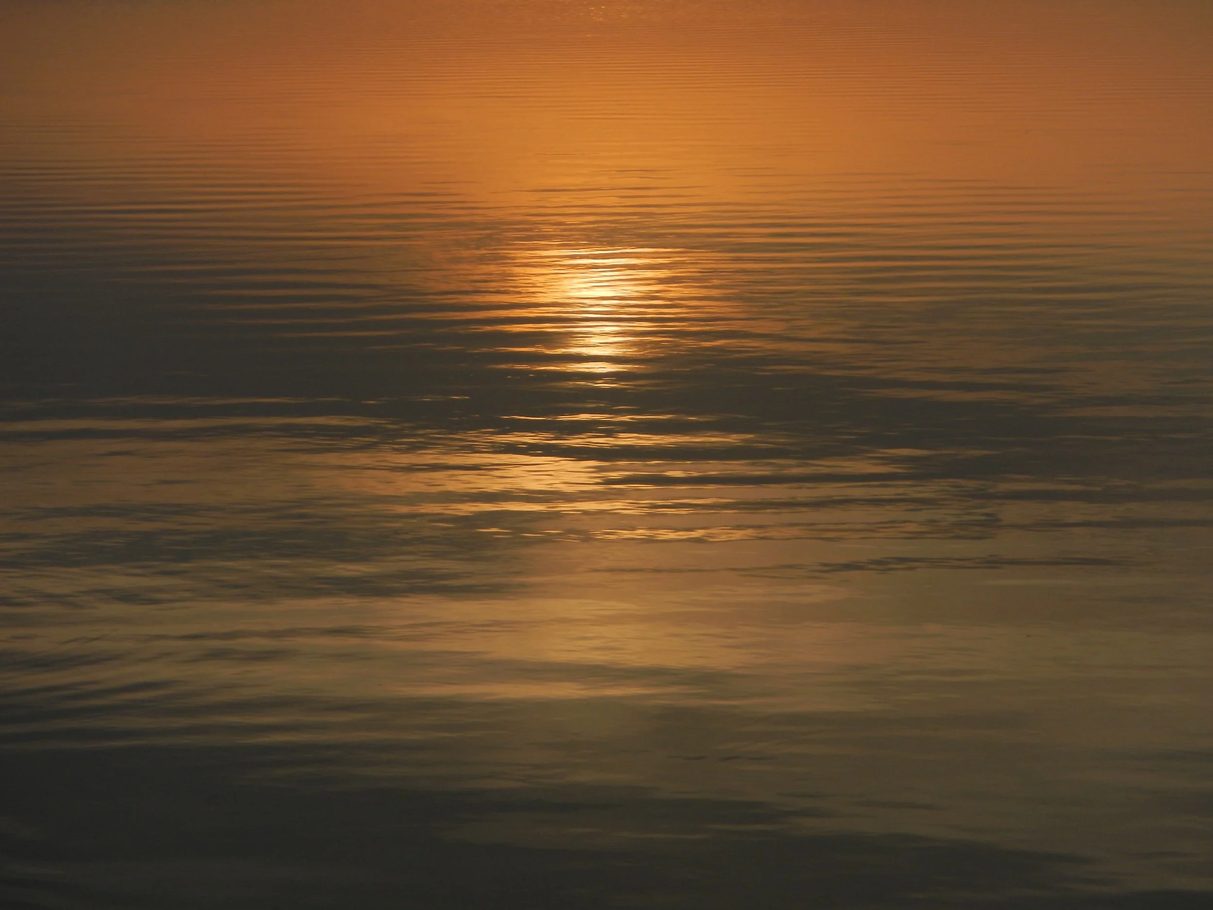 Sunset over calm water with reflections and gentle ripples