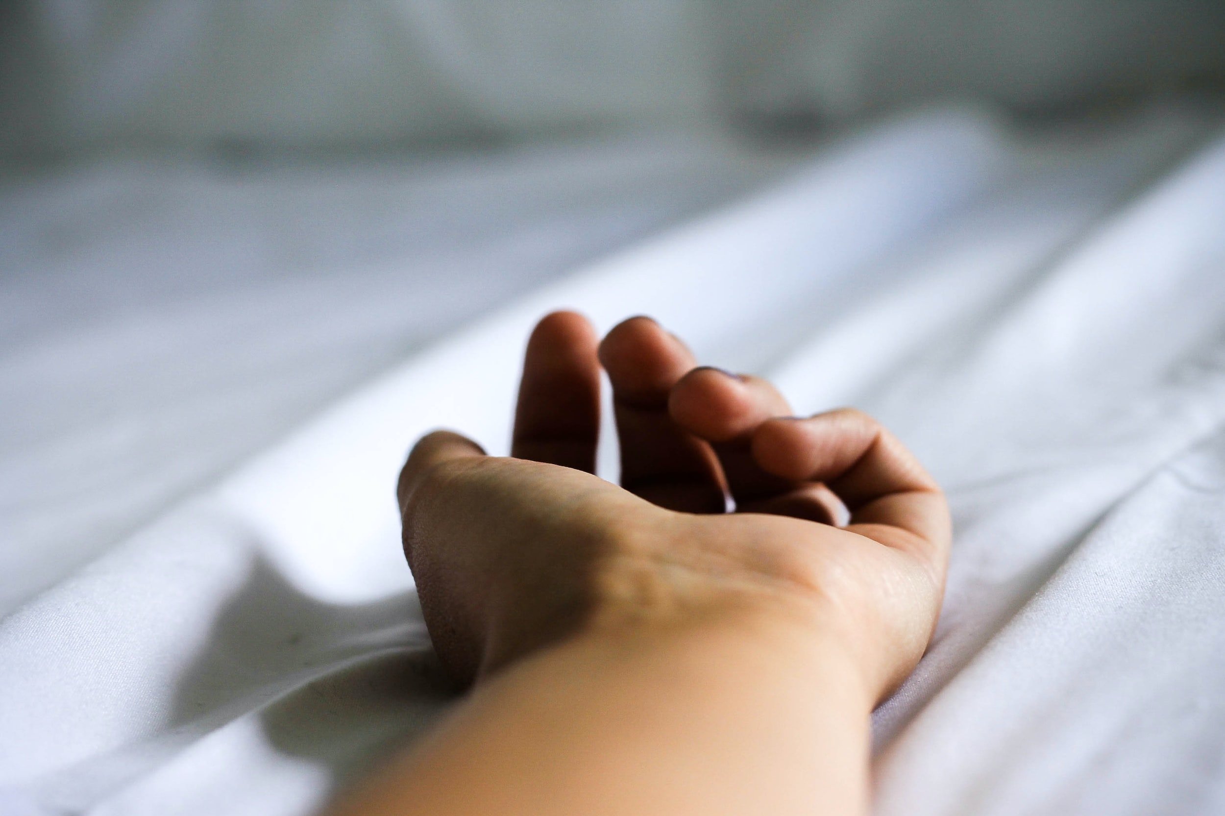 A person's hand gently resting on a white bed sheet.