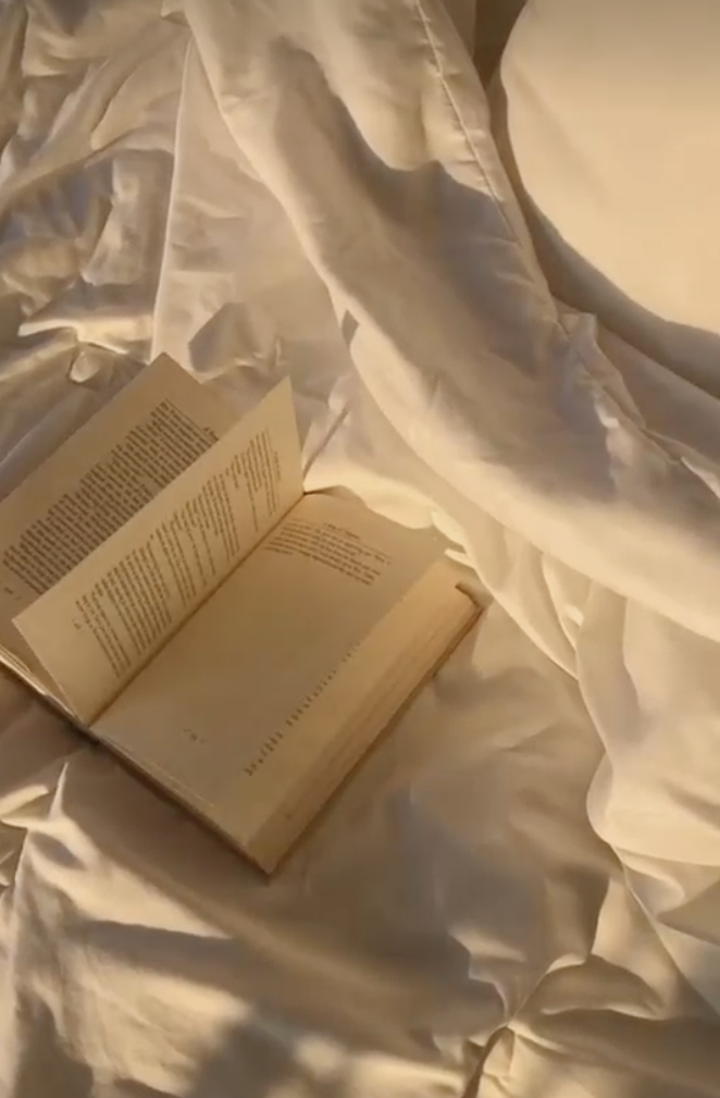 Open book lying on white satin bedsheets.