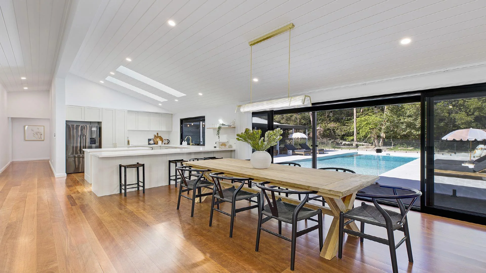 Open-concept kitchen and dining area with wood flooring, white cabinetry, and large sliding glass doors leading to an outdoor pool area.