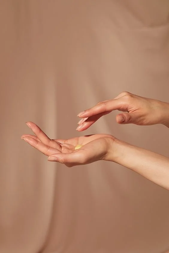 Two hands, one above the other, with the top hand about to grab a pill from the lower hand, against a beige background.