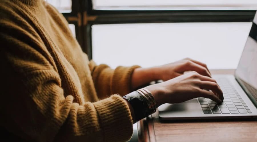 Person wearing a mustard-colored sweater taking KindCo's Trust Self-Assessment on a laptop at a wooden table.