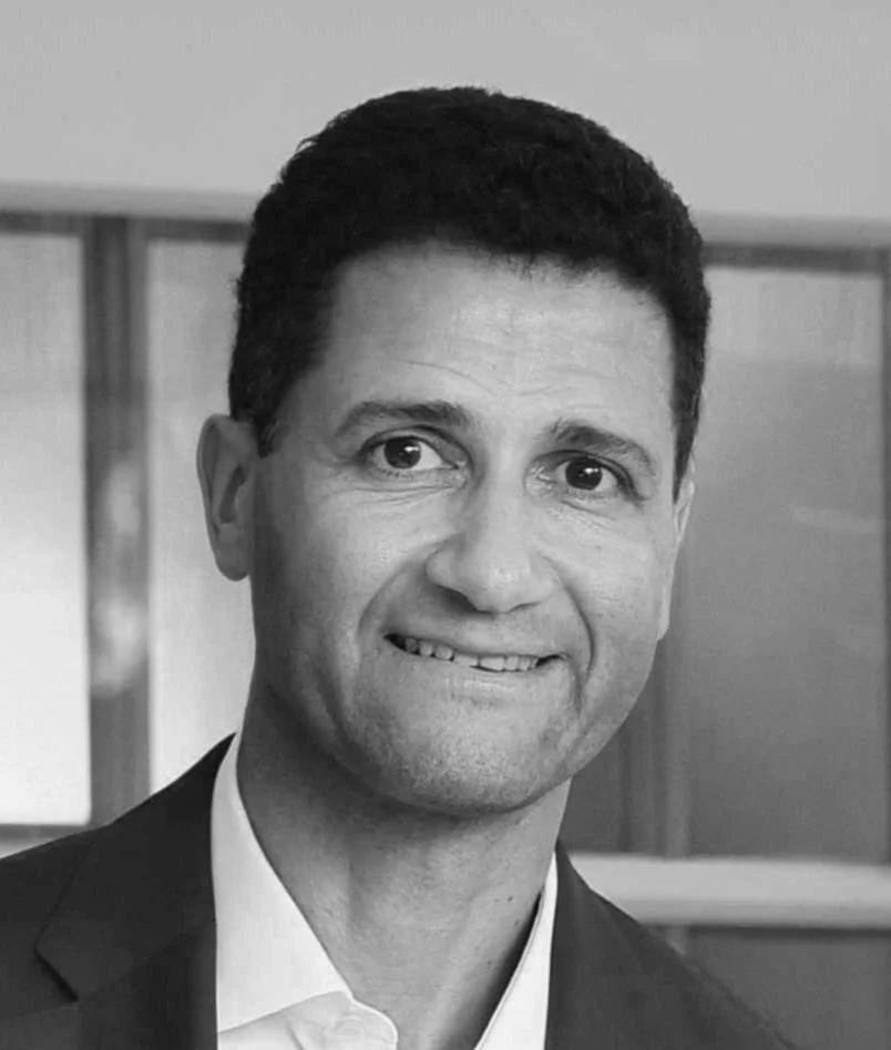 Black and white portrait of a smiling man in a suit, indoors.