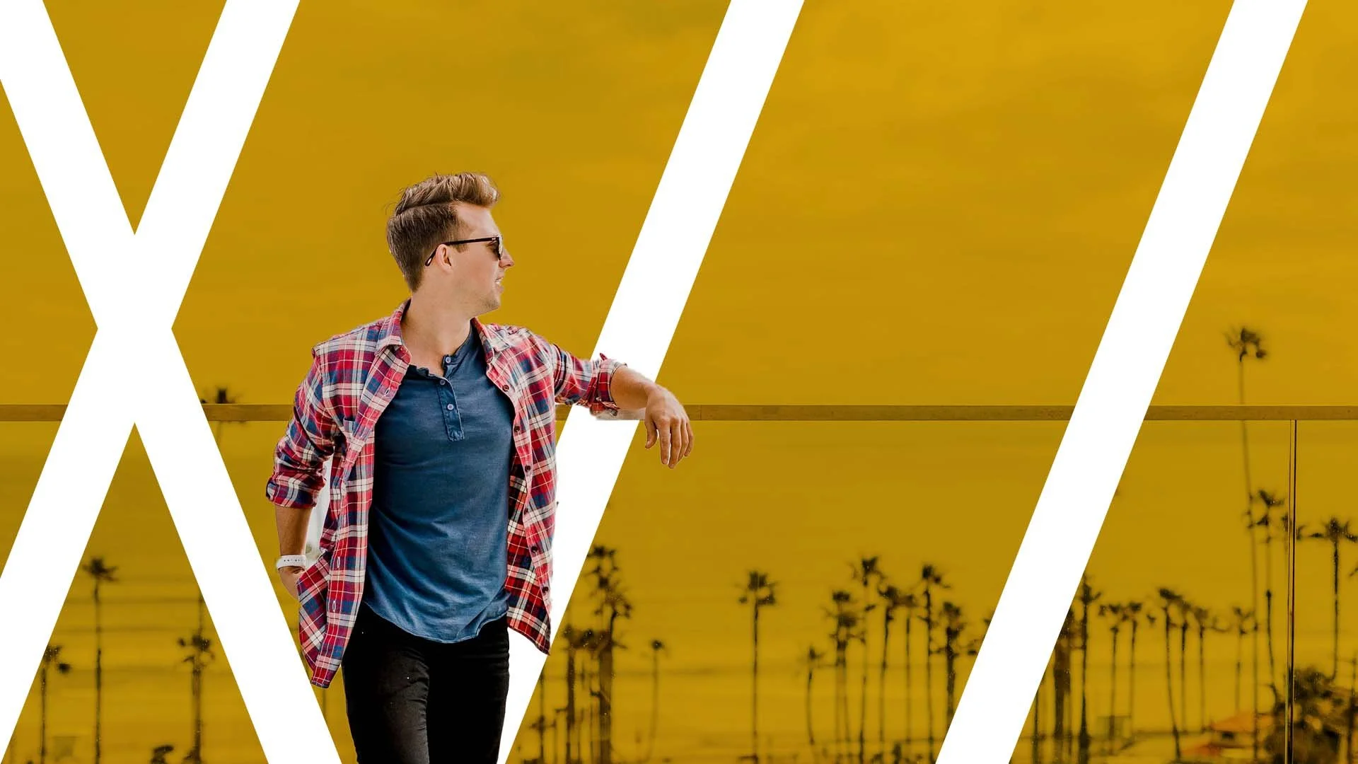 Man in sunglasses and plaid shirt standing against a yellow background with palm trees.