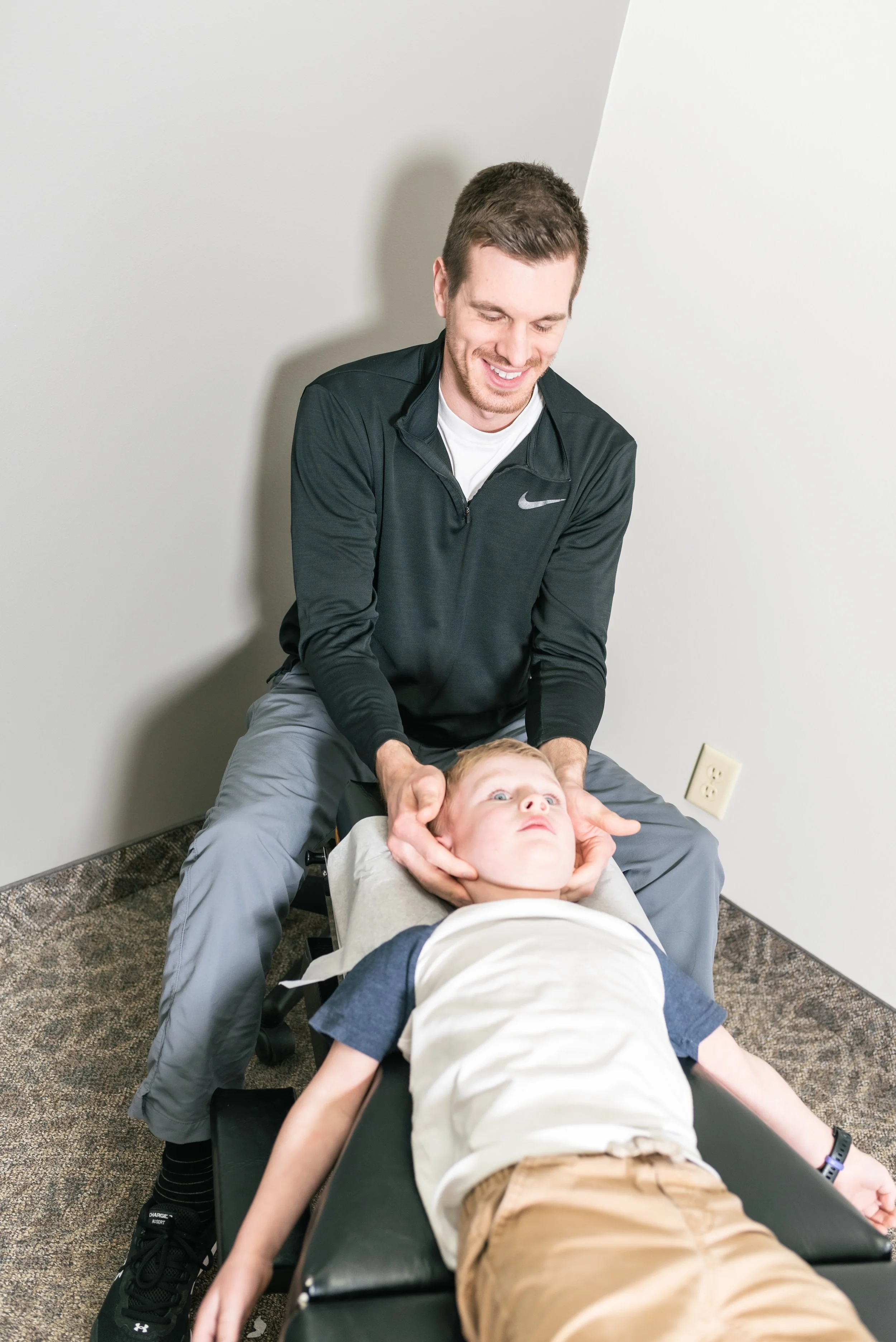 Practitioner sitting down while adjusting boy's neck
