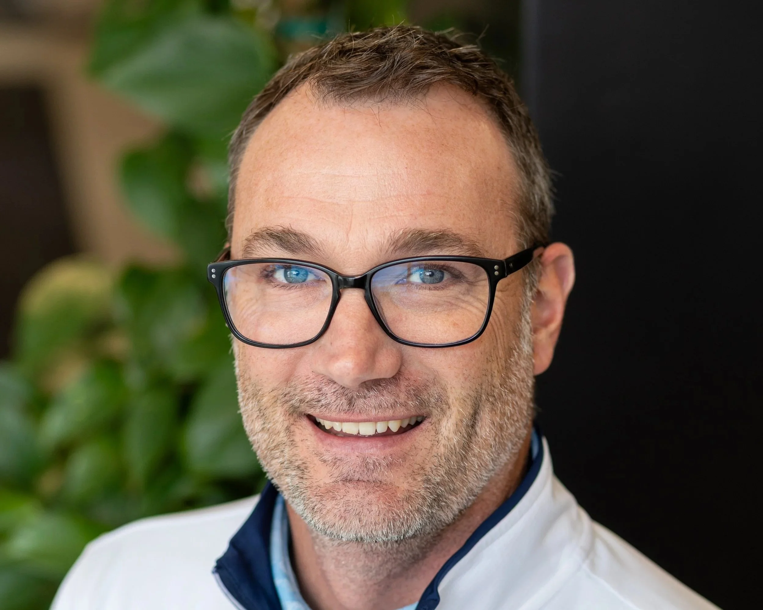 Man with brown hair, vest and smiling