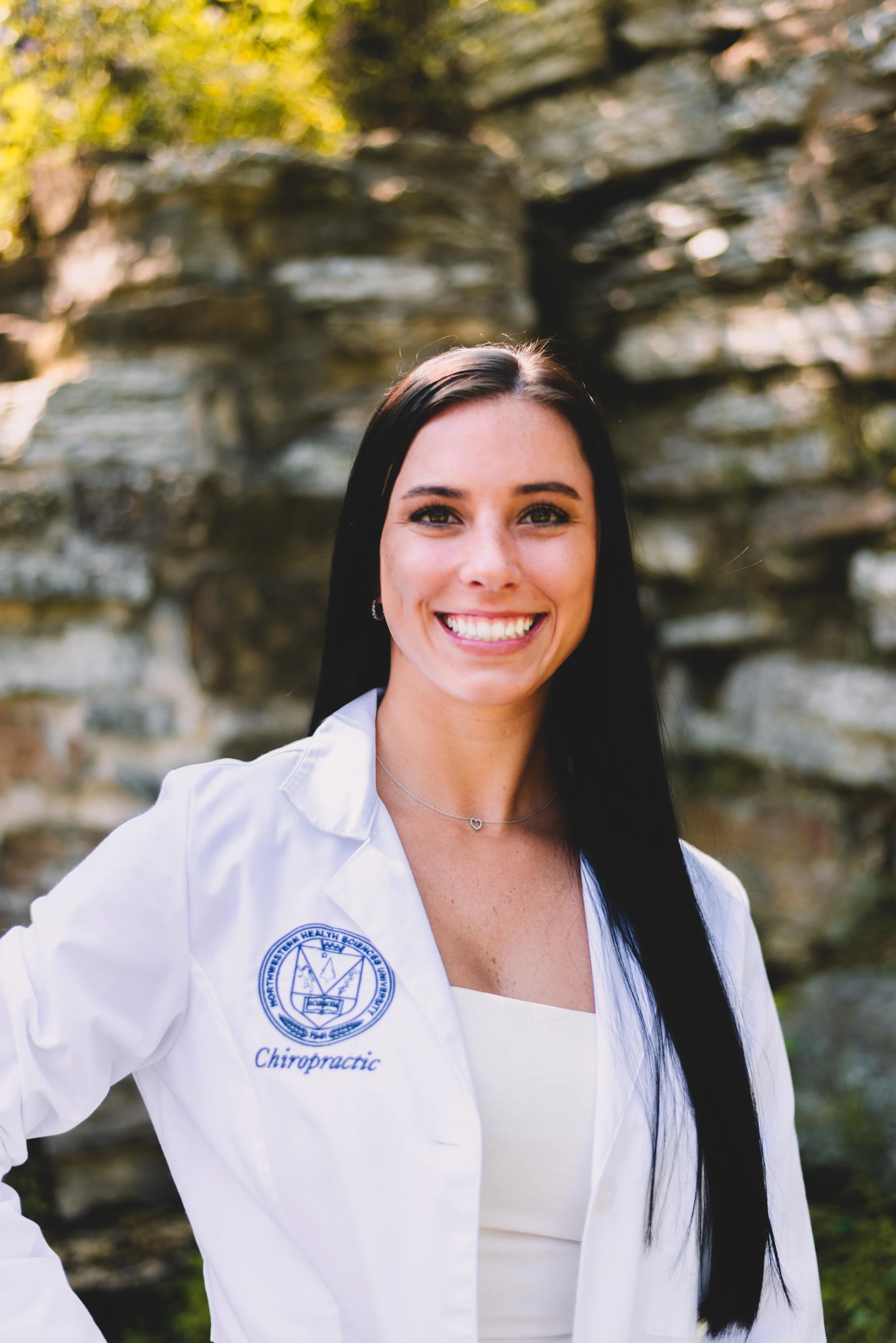 Smiling Woman in white lab coat with Chiropractic emblem on it with brown hair