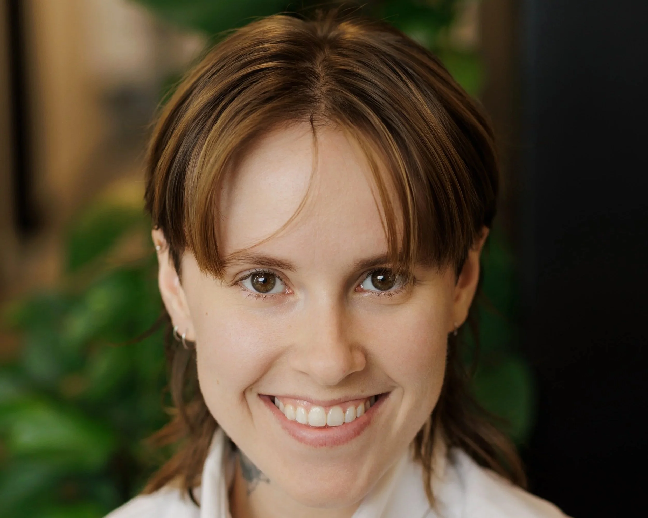 Smiling Woman with pixie haircut wearing denim blue shirt and silver chain around neck