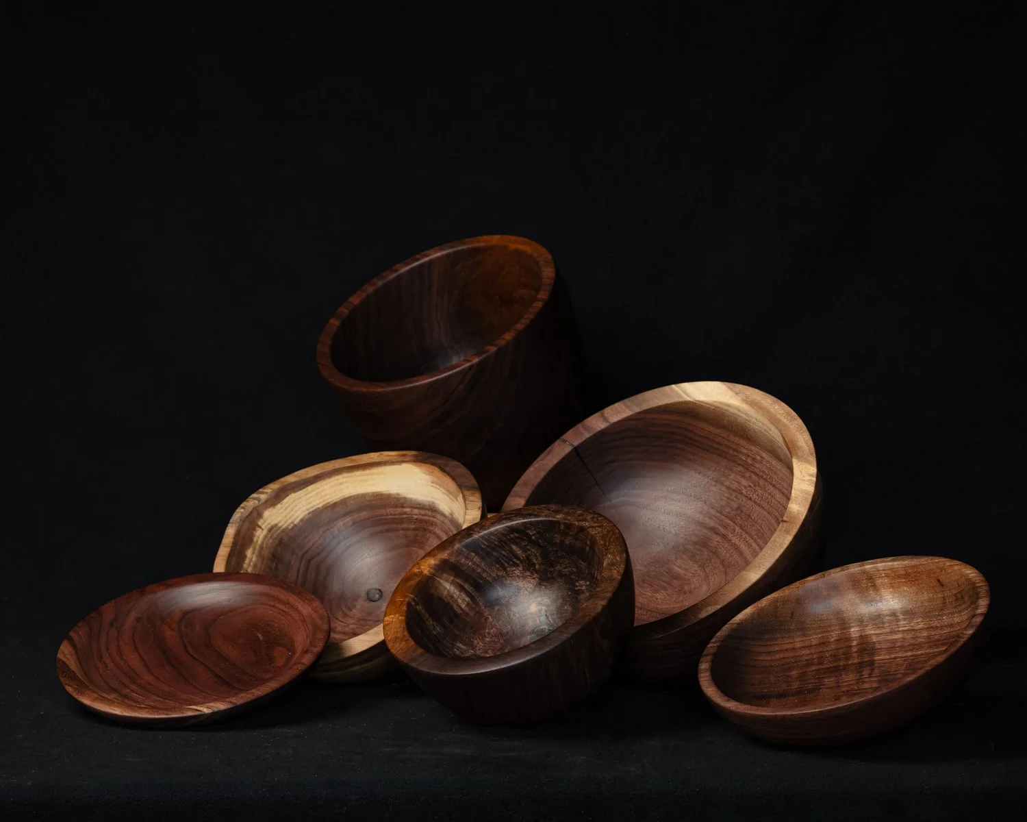 Several wooden bowls in various sizes and colors arranged on a dark background.