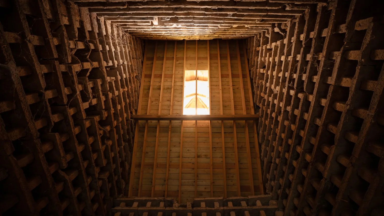 Interior view of a building under construction showing brick walls and a roof frame with a skylight letting in natural light.