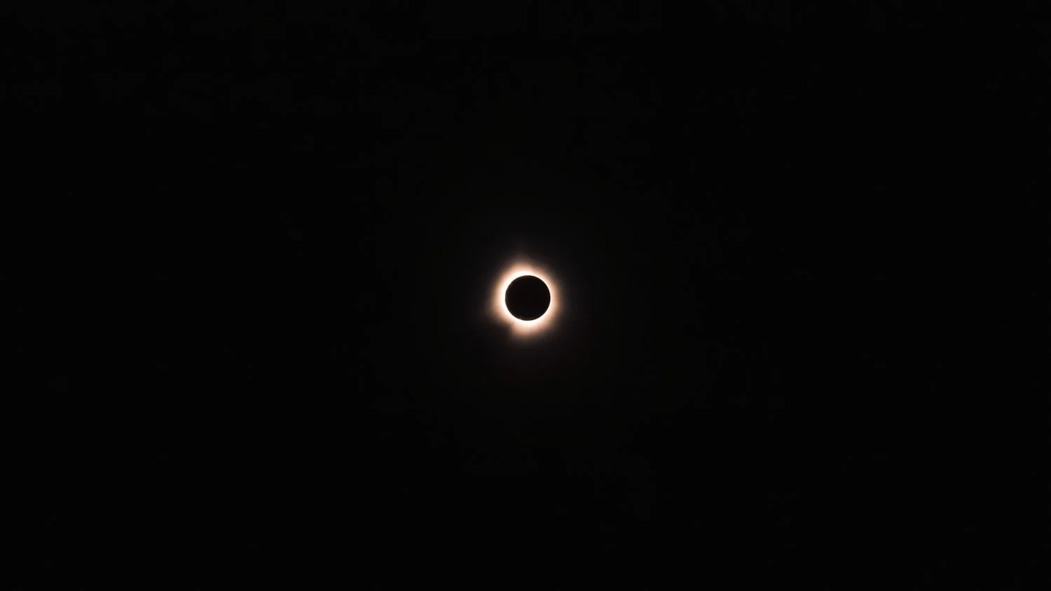 Photo of a solar eclipse showing the moon covering the sun with a glowing corona around the edges.