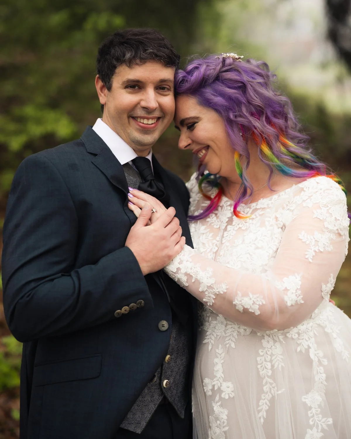 A happy couple in wedding attire sharing a tender moment outdoors surrounded by greenery.