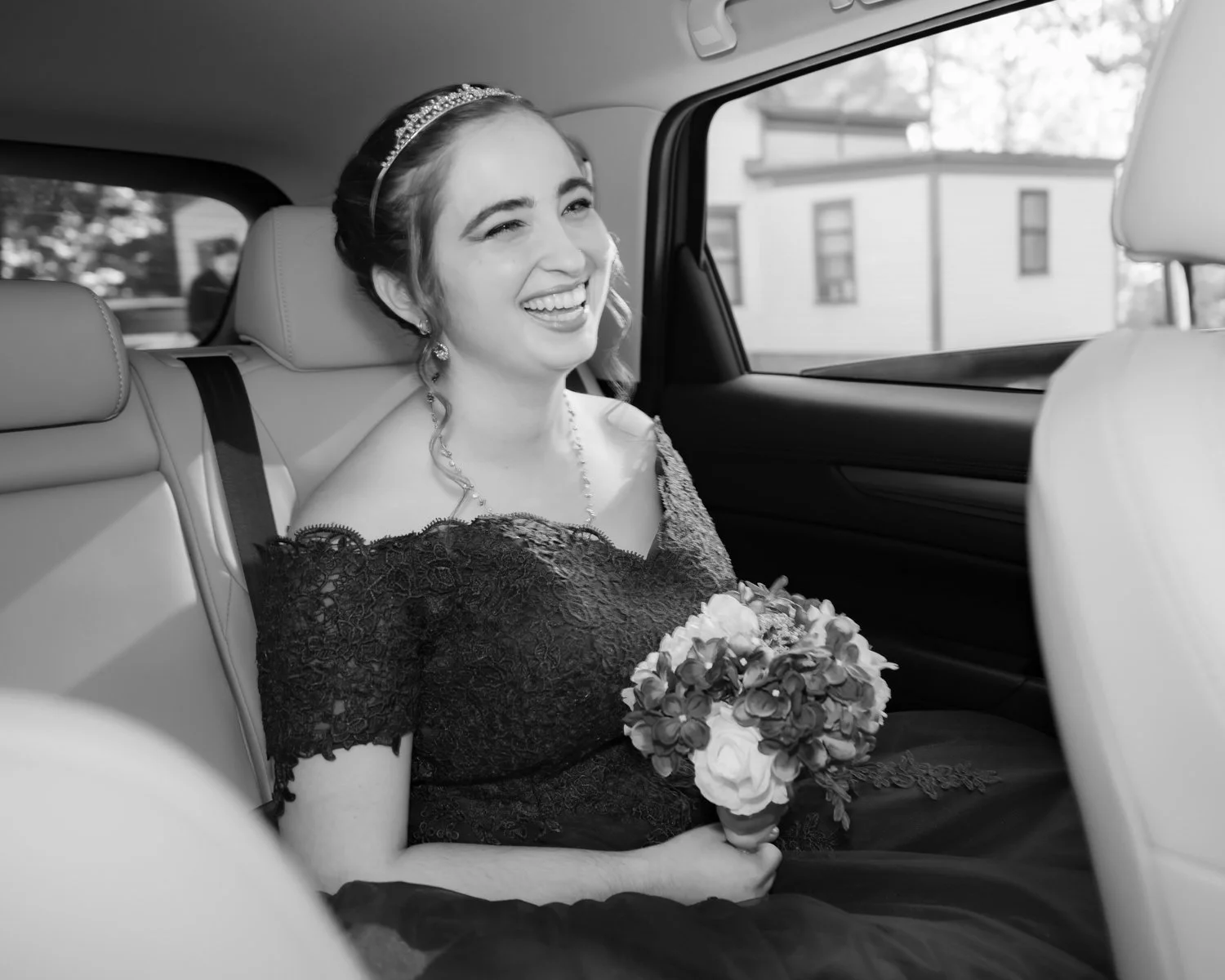 A smiling bride sitting in the backseat of a vehicle, holding a bouquet of flowers.