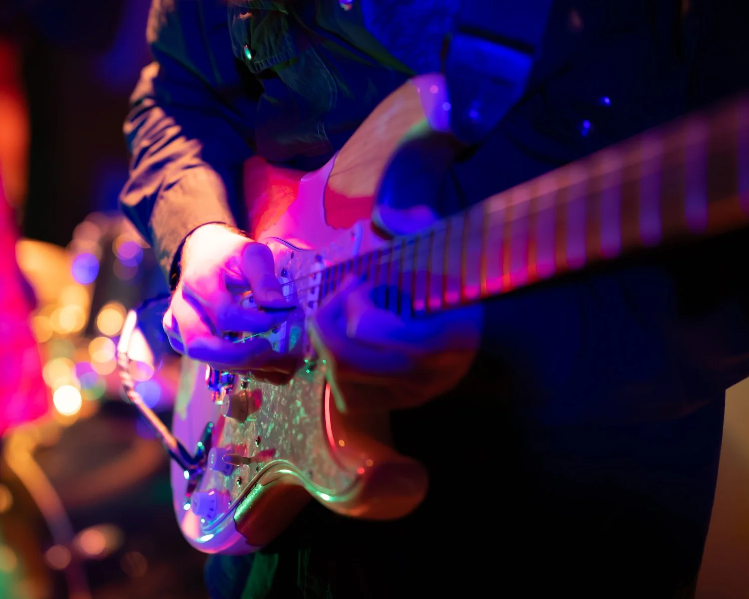 A person playing an electric guitar under colorful stage lights.