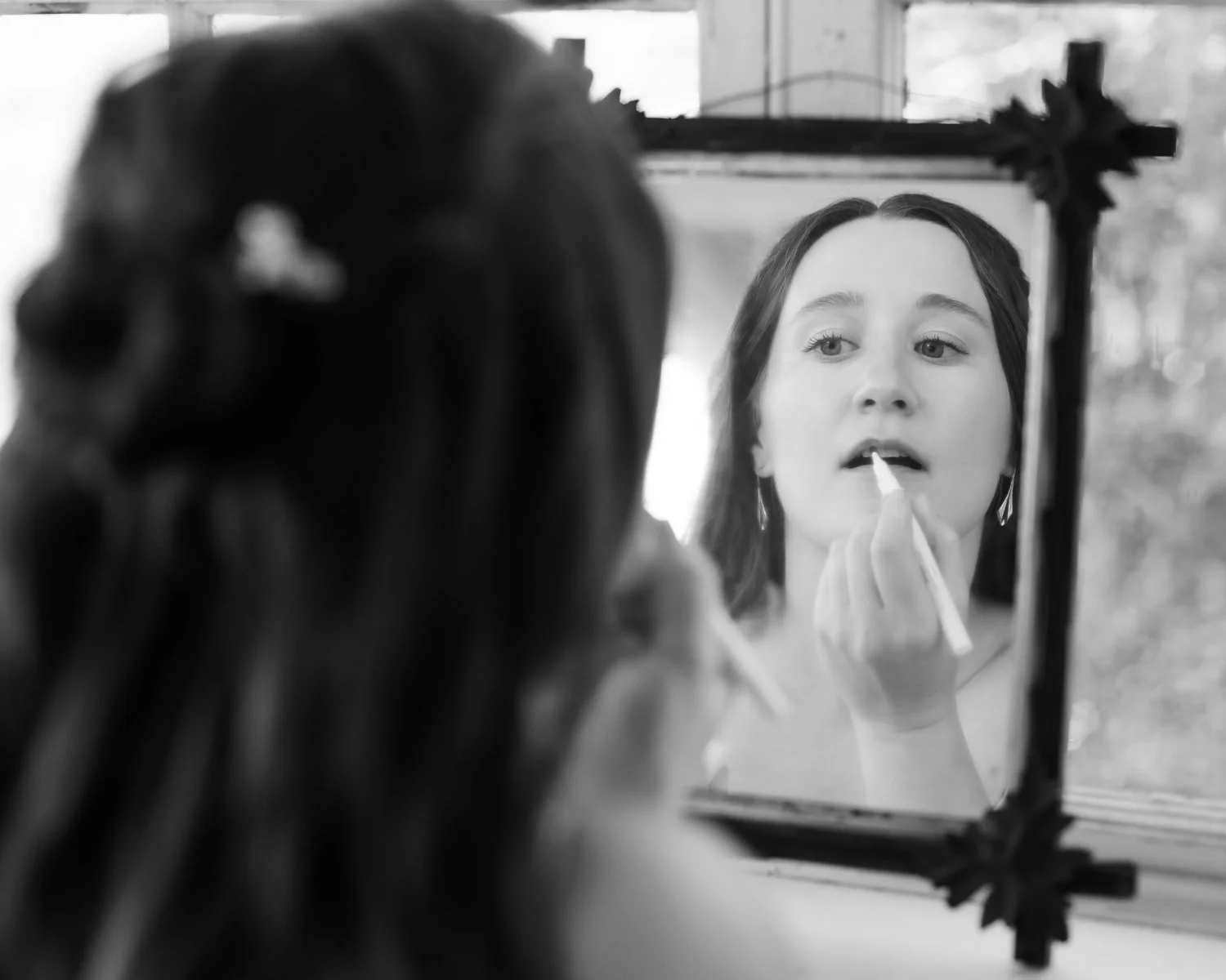 A woman applying lipstick while looking in a mirror.