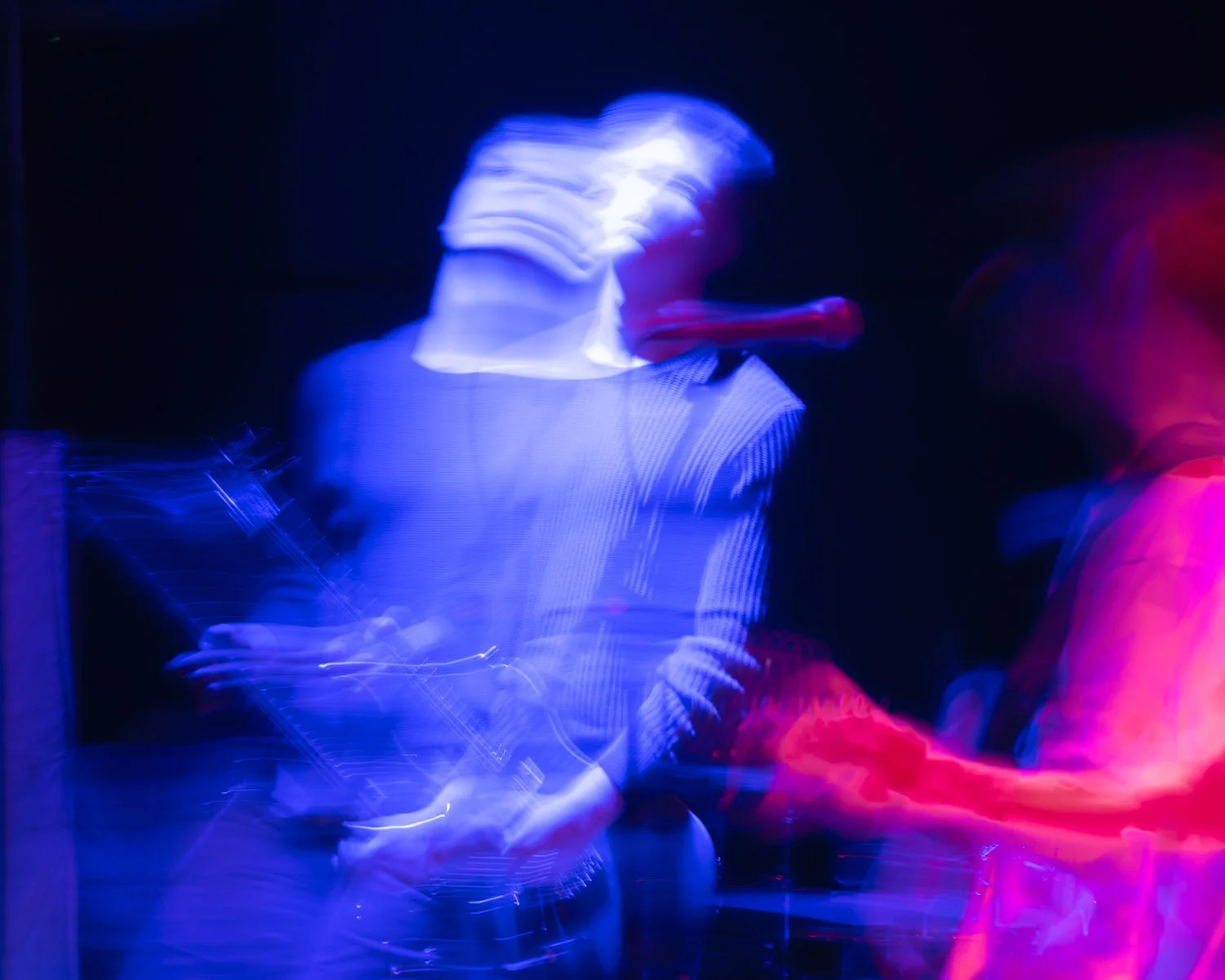 A musician playing an electric guitar with motion blur and vibrant blue and red stage lighting.