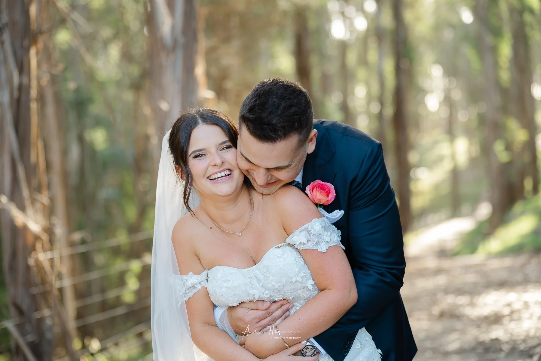 A bride and groom smiling and embracing in a wooded outdoor setting on their wedding day