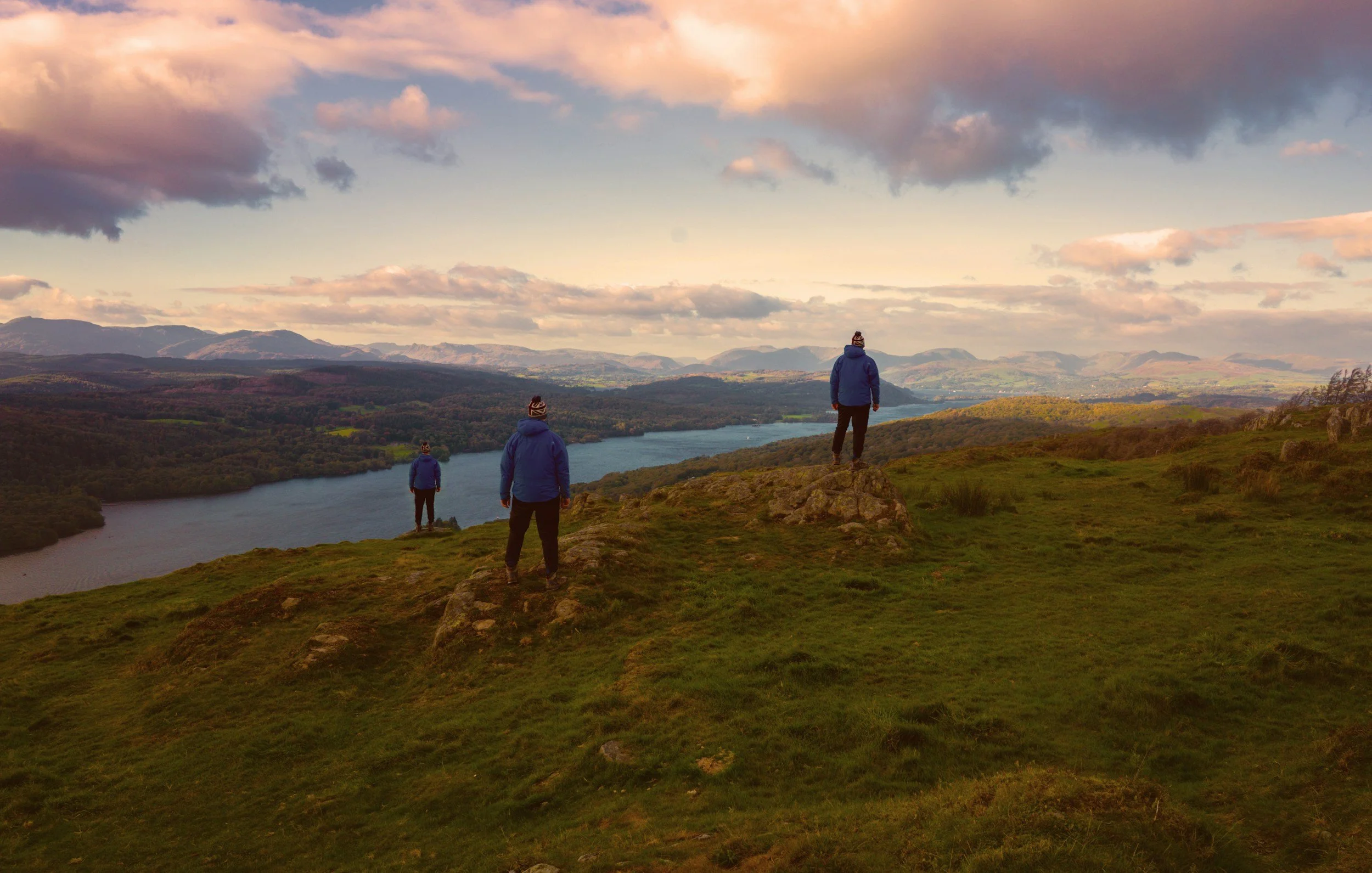 Silhouette d'une personne debout sur un rocher au lever du soleil avec les bras écartés, devant une chaîne de montagnes.