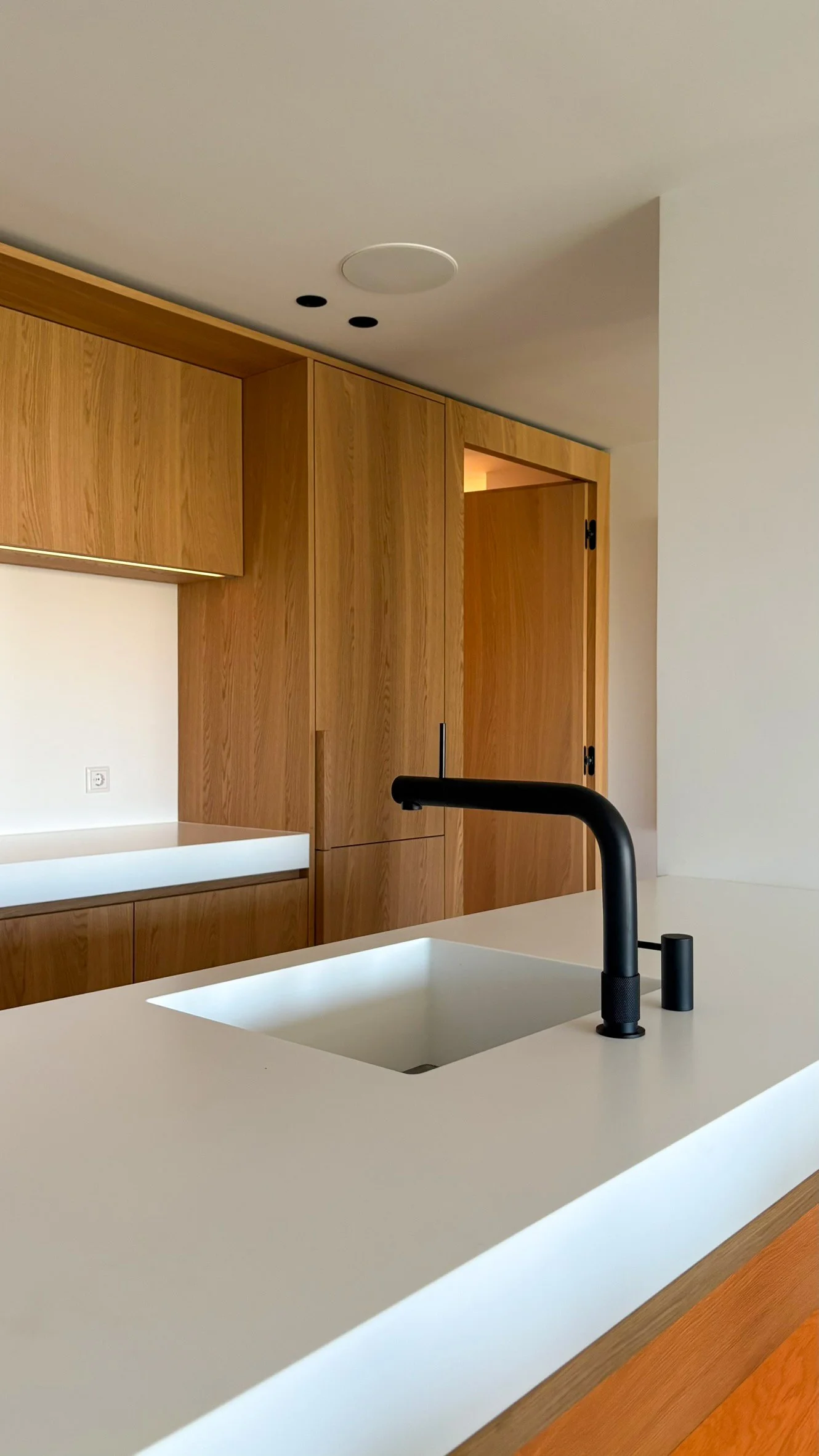 Modern kitchen with a white countertop, black faucet, wooden cabinets, and a built-in sink.
