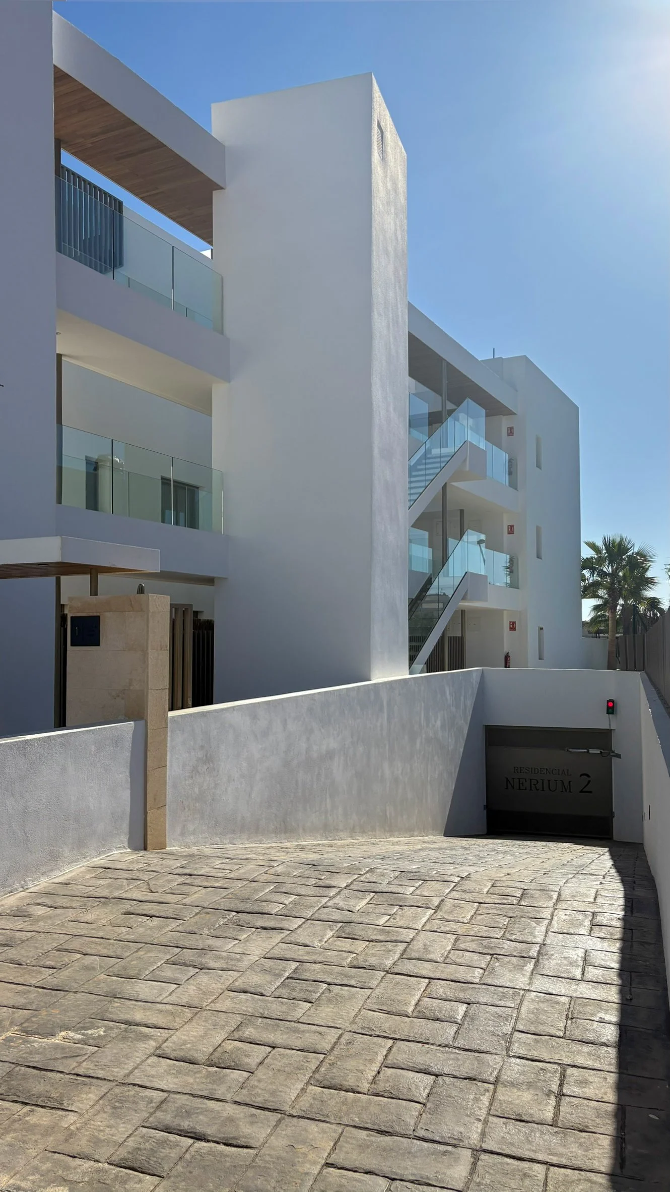 Modern white residential building with glass balcony railings, staircases, and a clear blue sky.