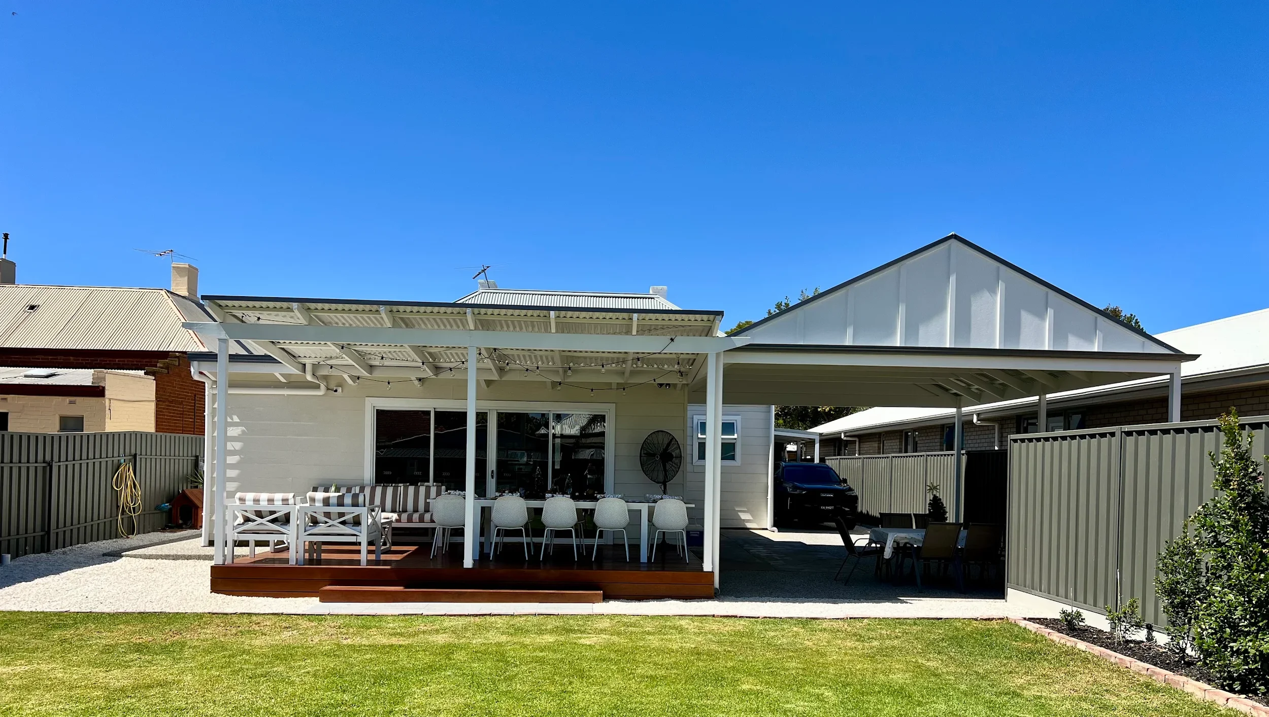 Residential backyard with a covered outdoor dining area, patio furniture, and a green lawn. Gable veranda.