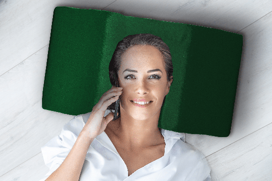 Woman lying on floor, talking on phone, wearing white shirt, green pillow.