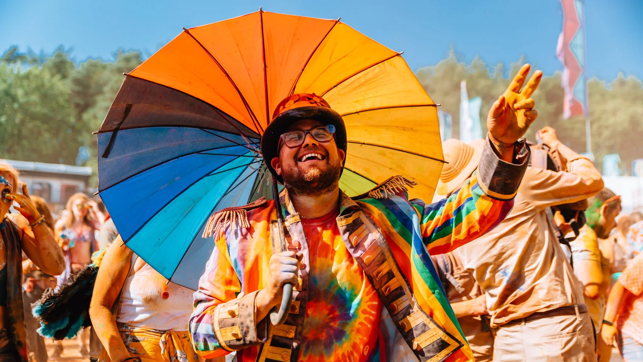  a man with a Rainbow umbrella and outfit dance at a music festival.