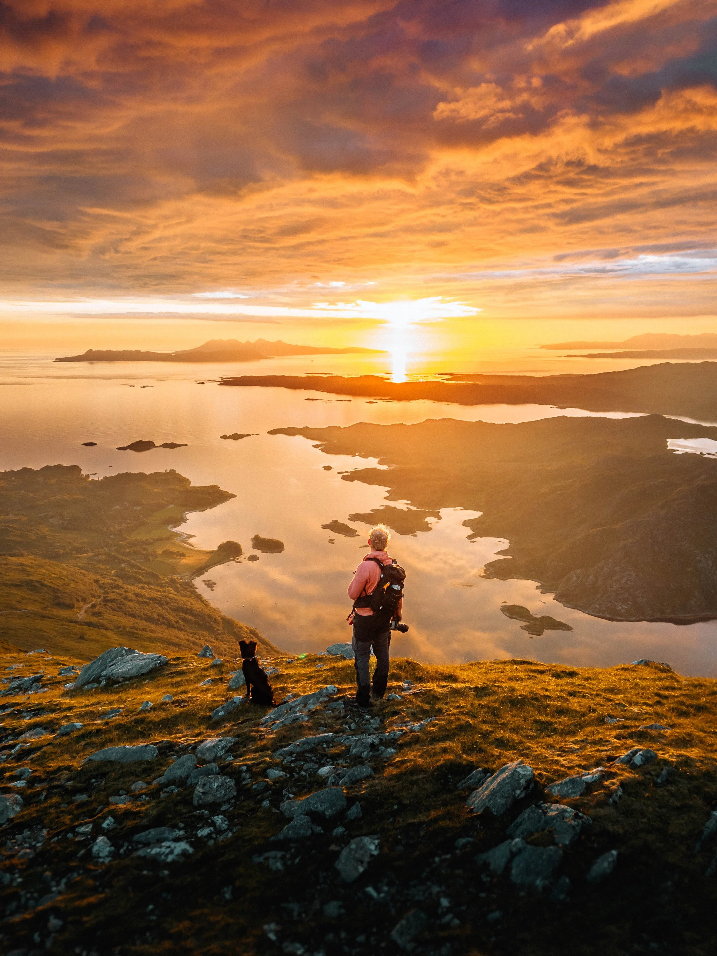  manin dog stand in the sunset on mountain overlooking Loch Ailort, Scotland. Rois-Bheinn