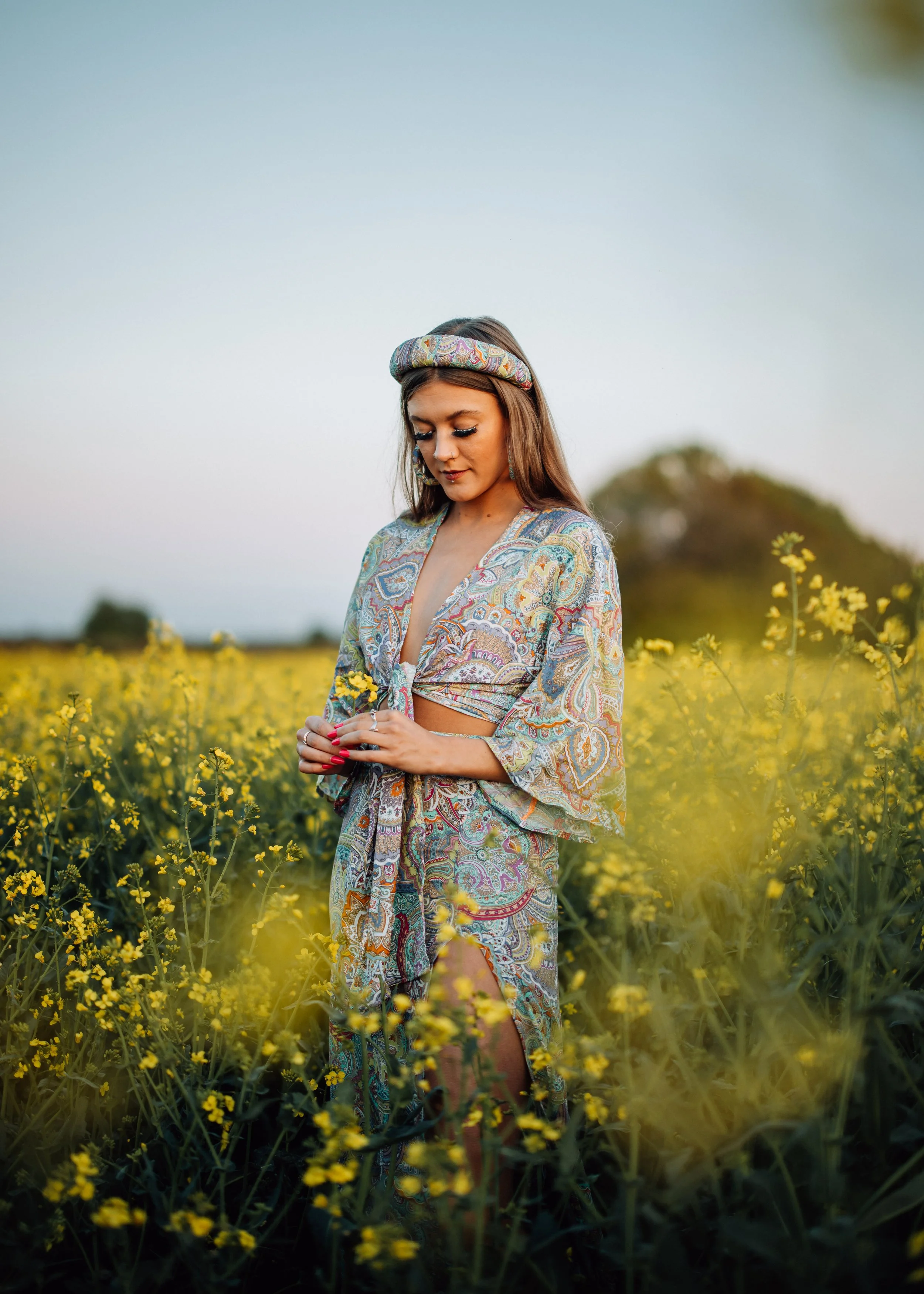  girl in hippie outfit stands and field of yellow flowers