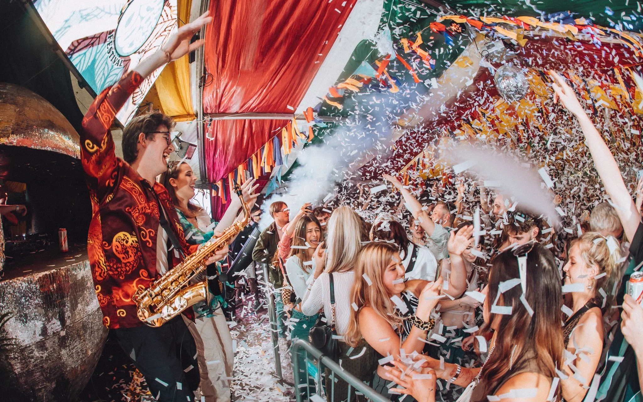 a man plays the saxophone to a huge crowd. There is confetti in the air.