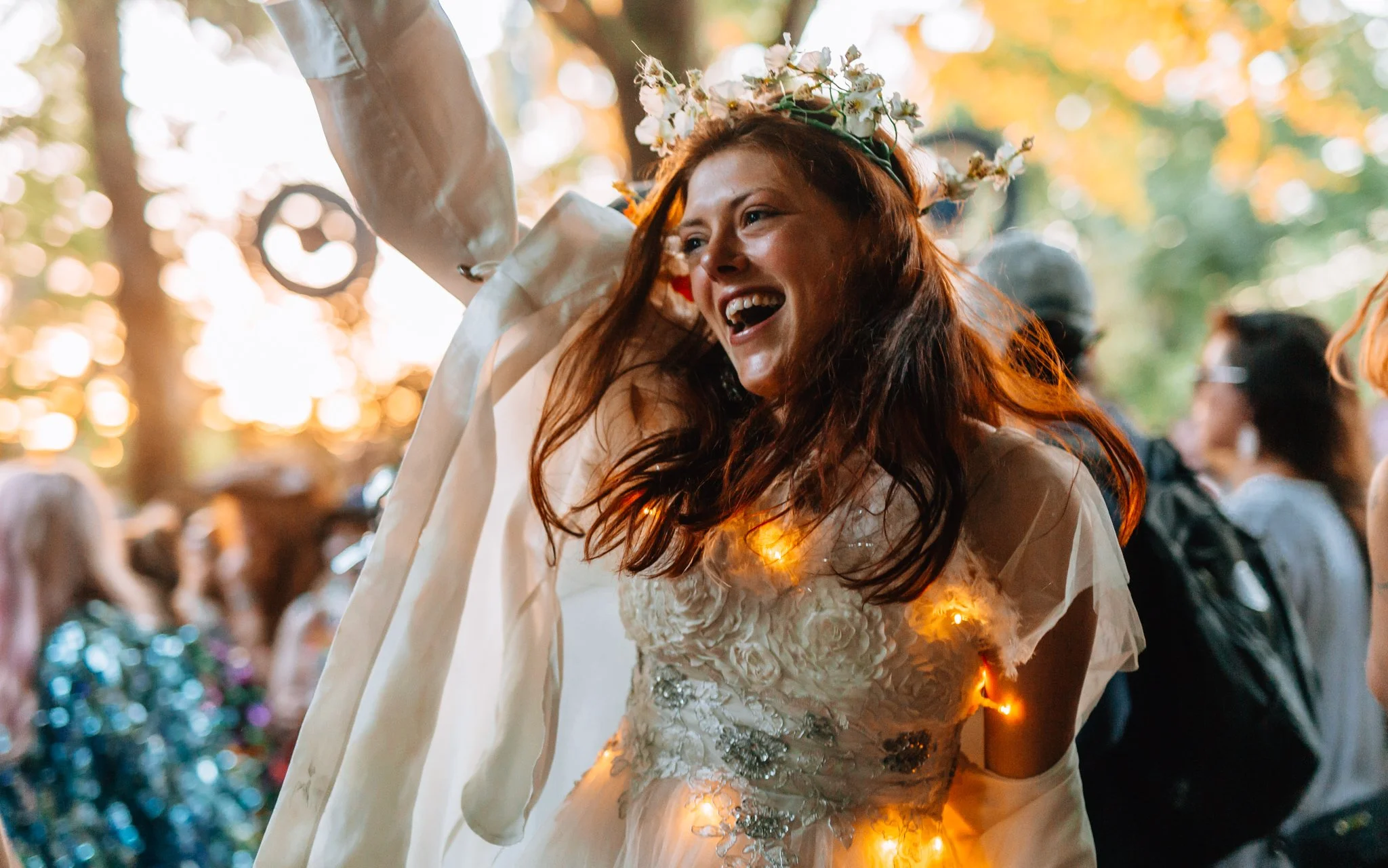  a girl with a flower garland and fairy lights dances at a music festival in the sunset