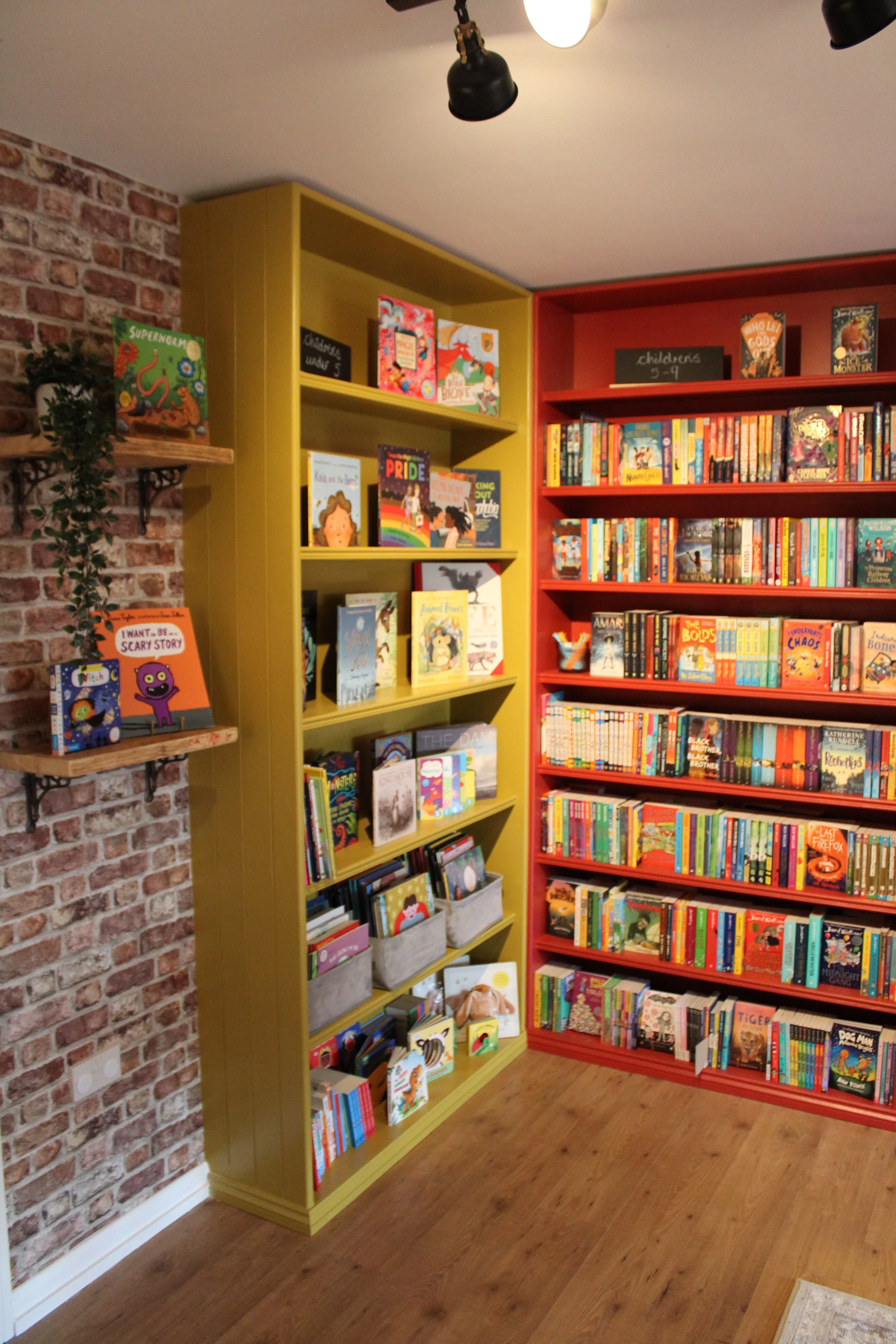 Bookshelves filled with children's books in a bookstore or library, with a small chalkboard sign labeled 'children's 3-9' on top.