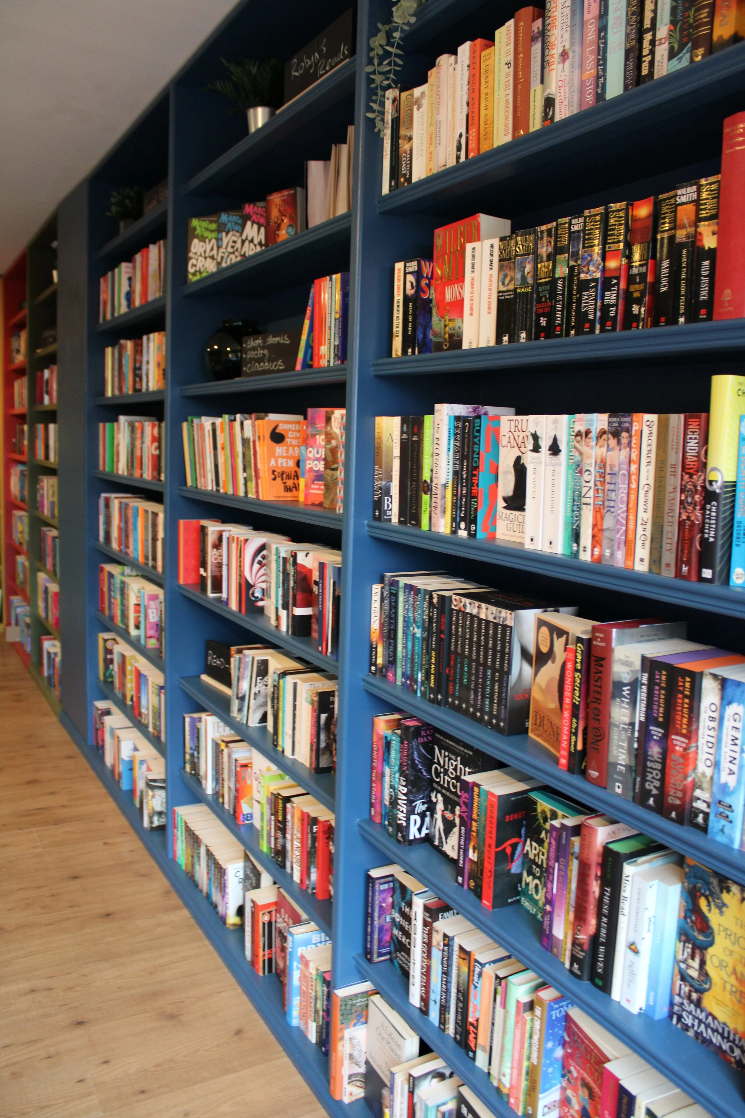 Blue bookshelves filled with a variety of colorful books on a wooden floor in a bookstore or library.