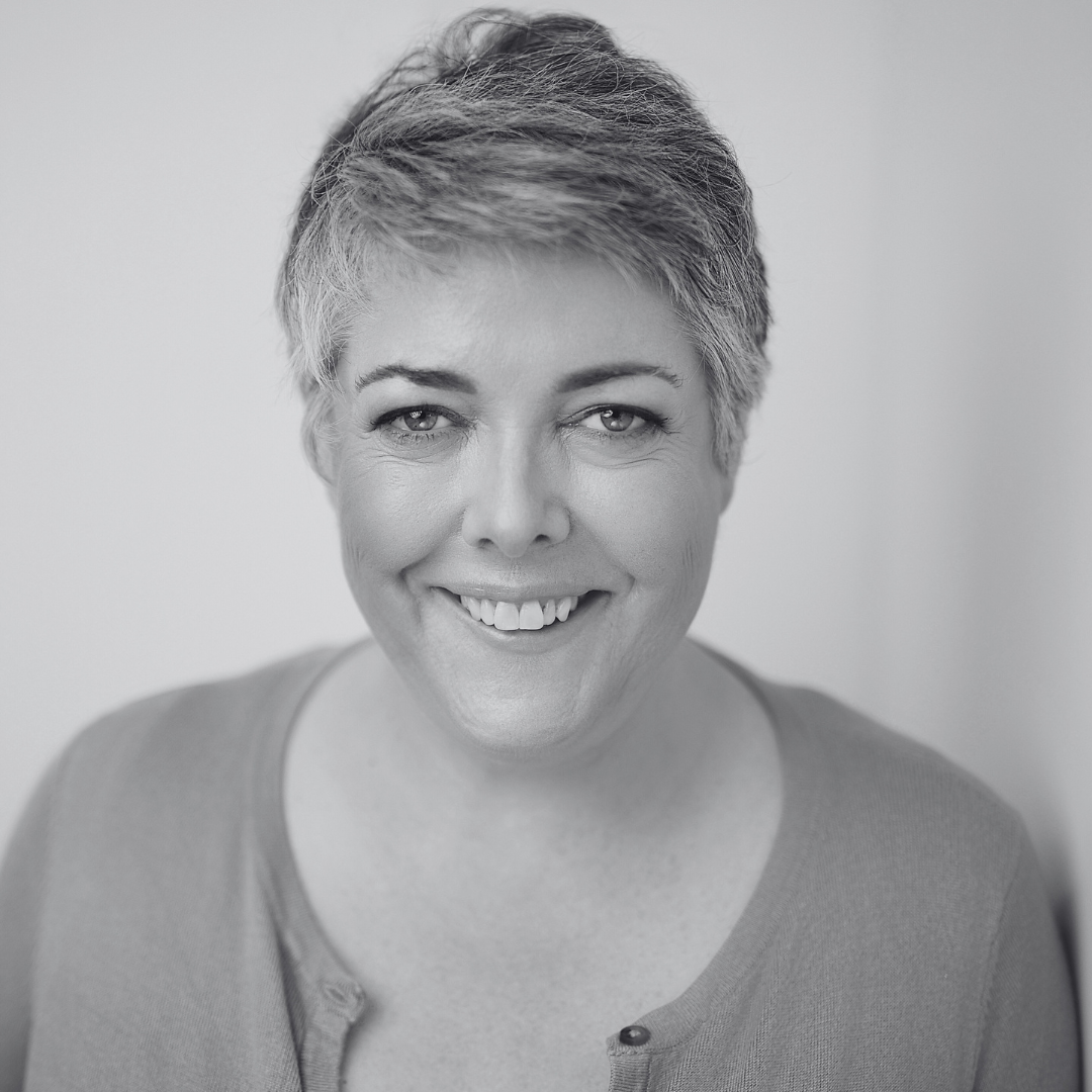 Black and white portrait of a smiling woman with short gray hair, wearing a round-neck shirt with a button detail.