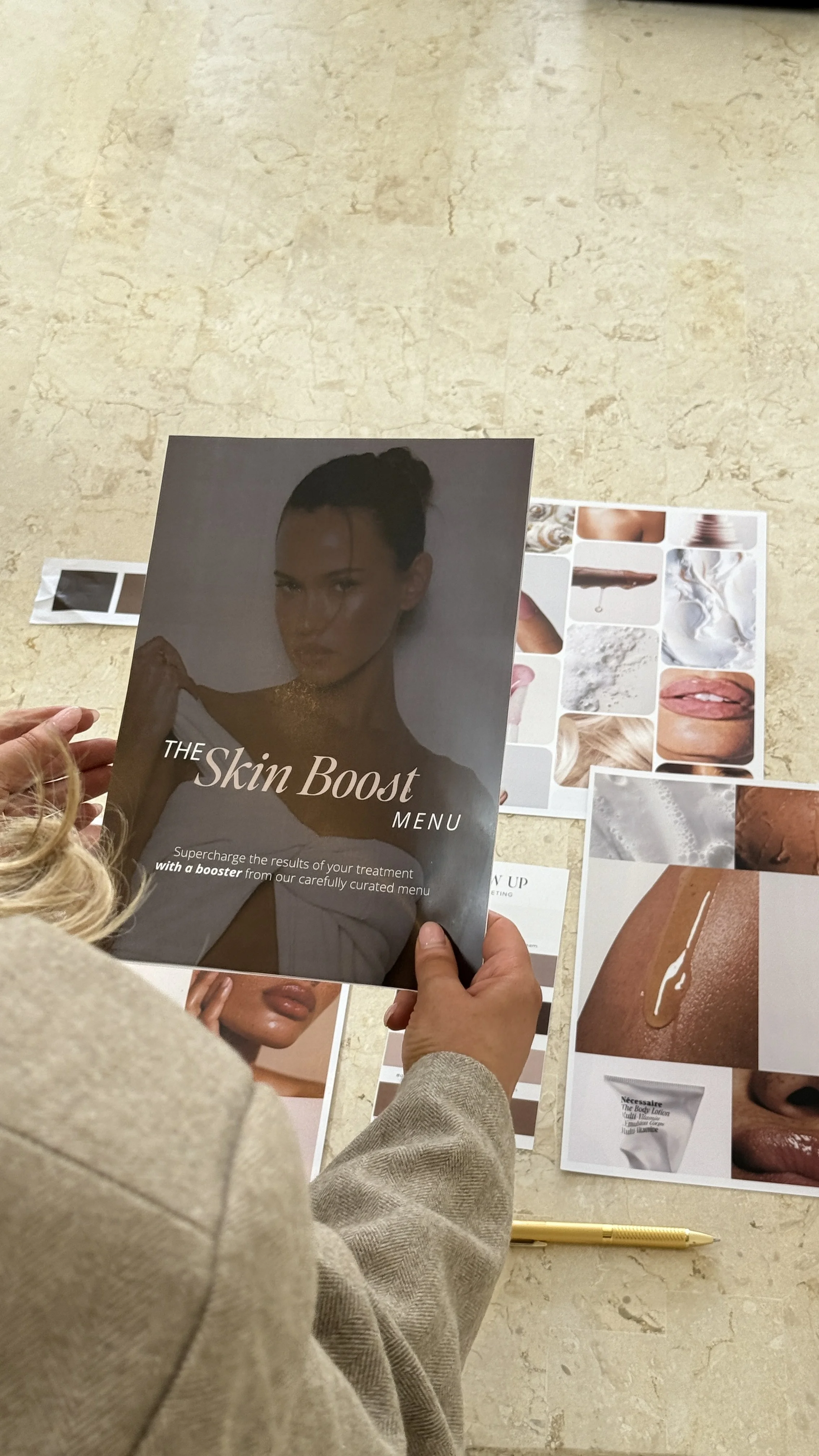 Person holding a beauty treatment menu titled 'The Skin Boost Menu,' with various skincare images and products on the table below.