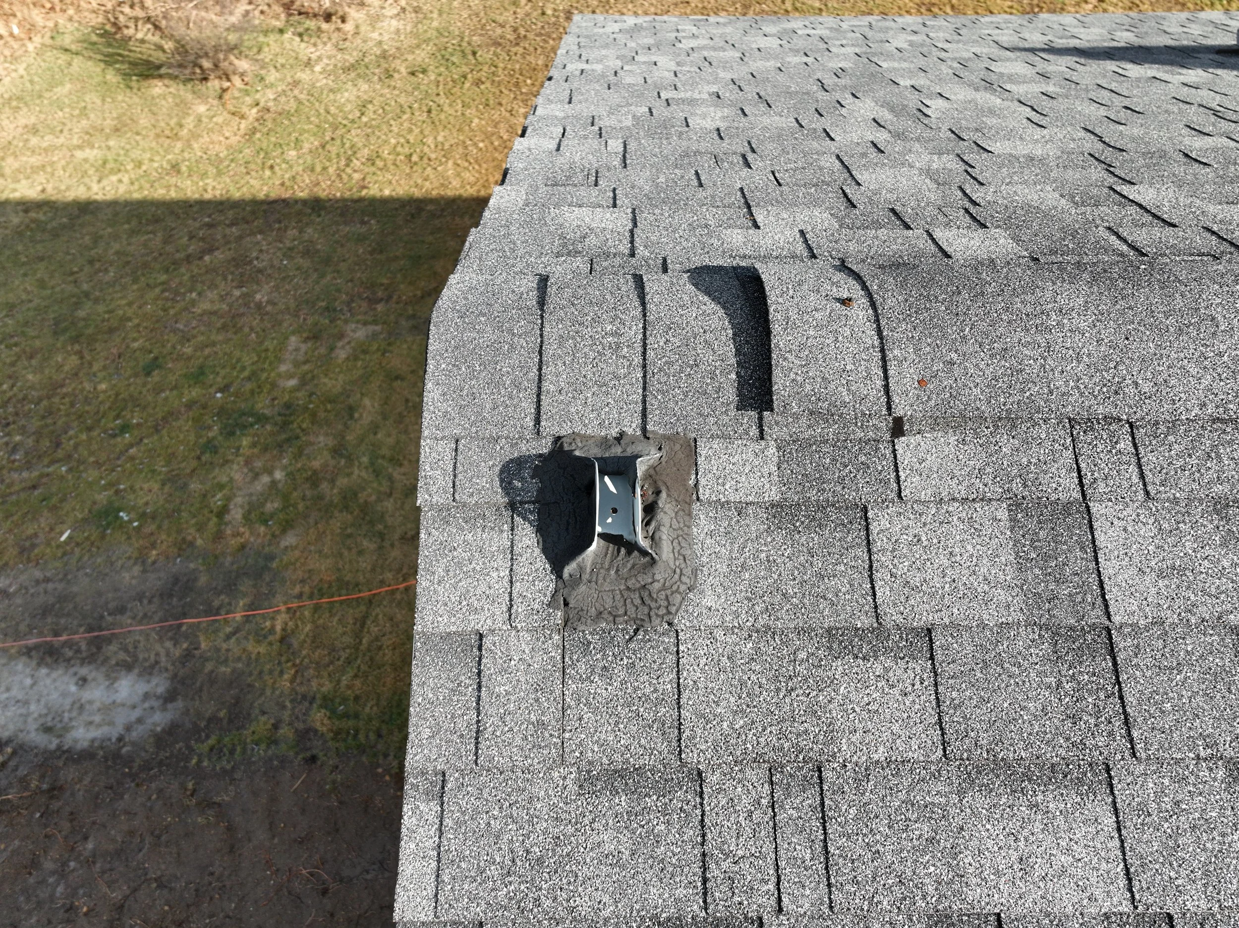 Close-up of a damaged roof with missing shingles and a broken vent pipe flashing on a gray asphalt shingle roof.